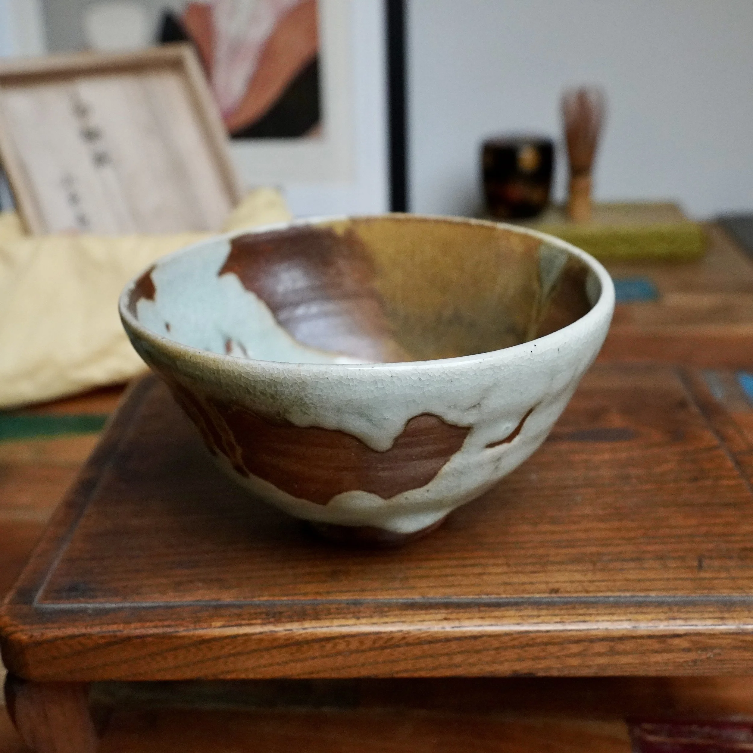 Sansōan chawan featuring pale blue-grey crackle glaze flowing into rust-brown, with ochre tones inside, on wood.