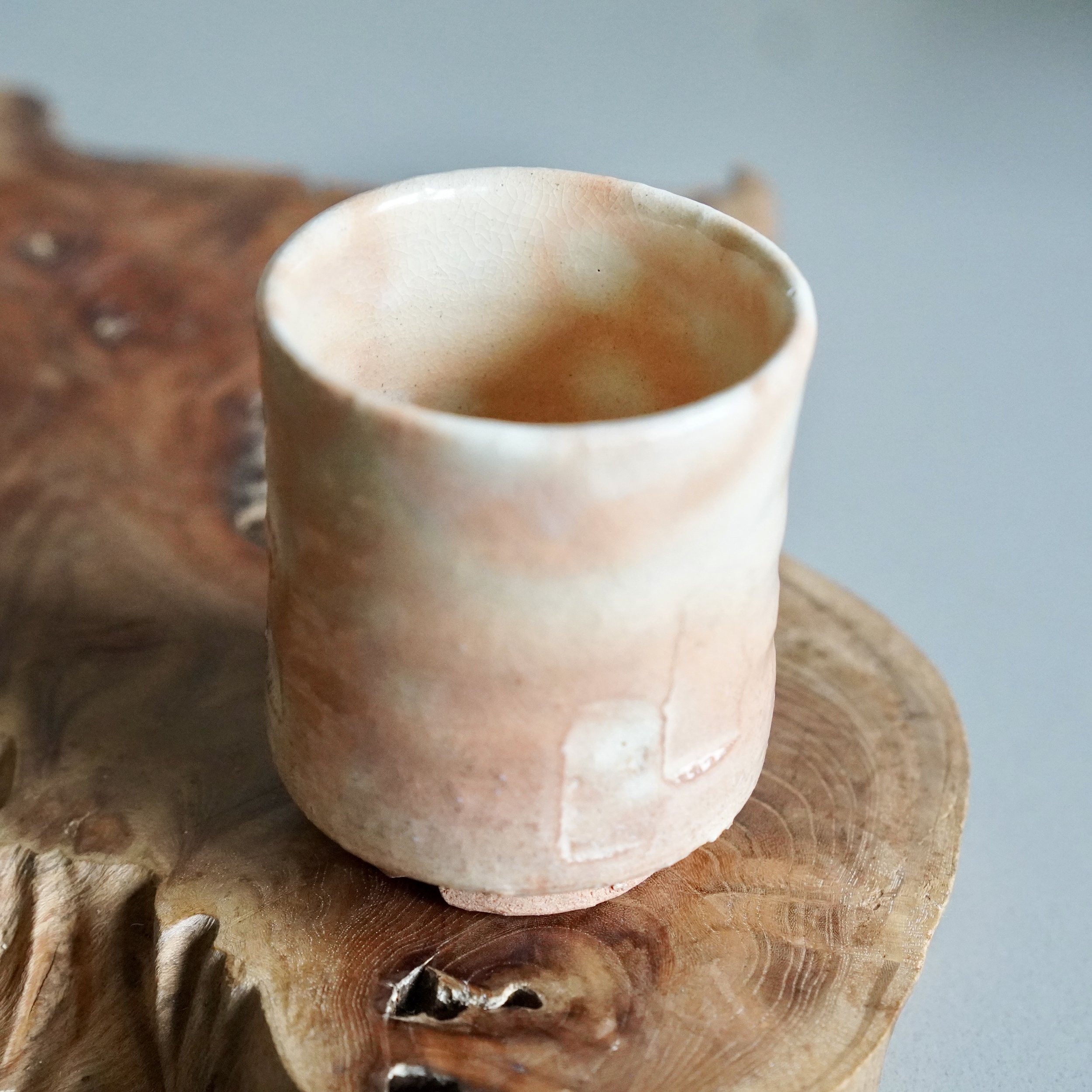 Vintage Japanese Hagi-yaki yunomi tea cup in unglazed natural clay with warm pink and orange tones from the kiln, on a wooden surface. Porous stoneware that develops patina with use, sourced in Japan.