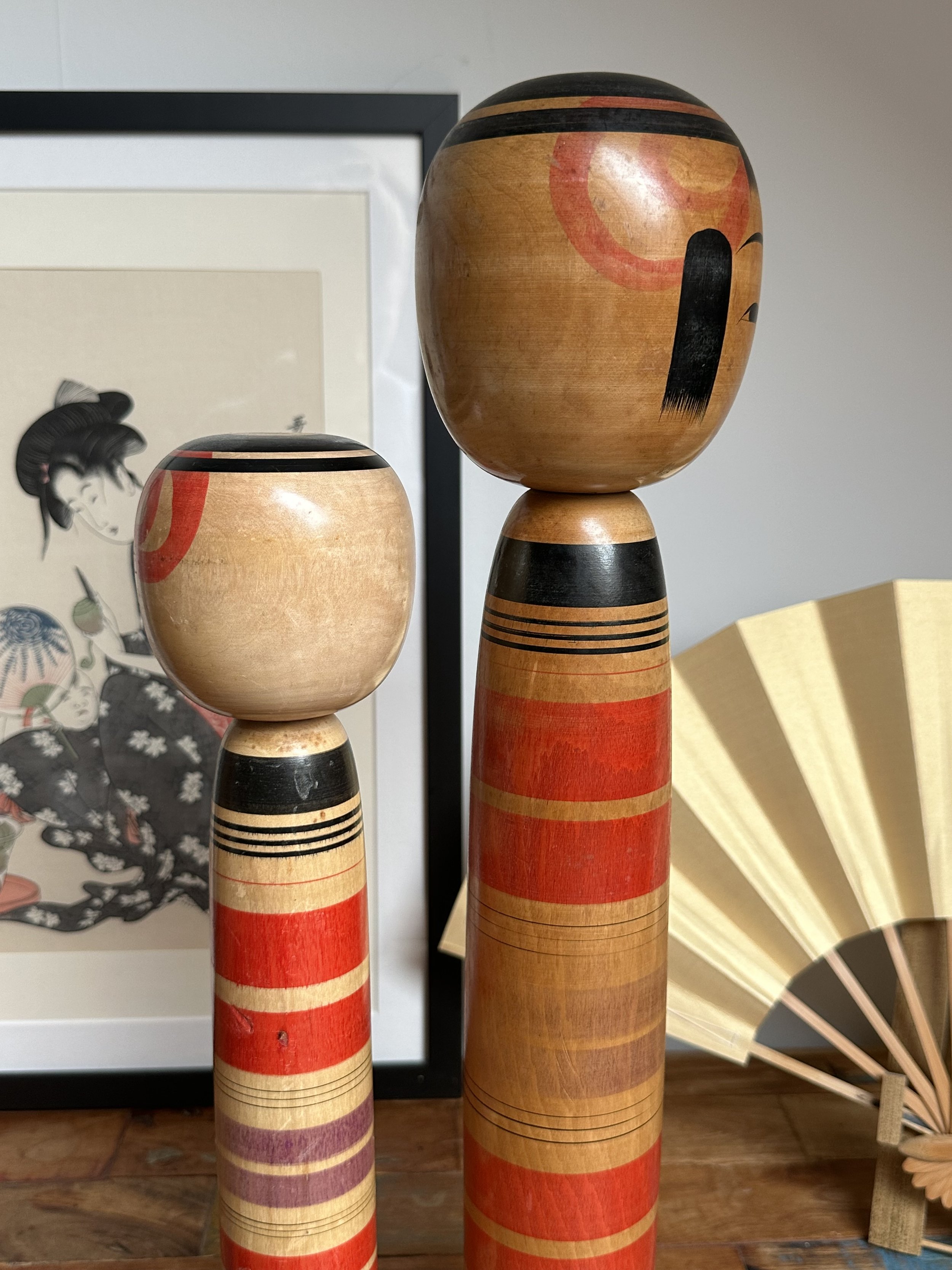 Pair of Abe Ichirō Tsuchiyu kokeshi, the taller with painted black facial features, both featuring traditional red, black, purple, and natural wood bands.
