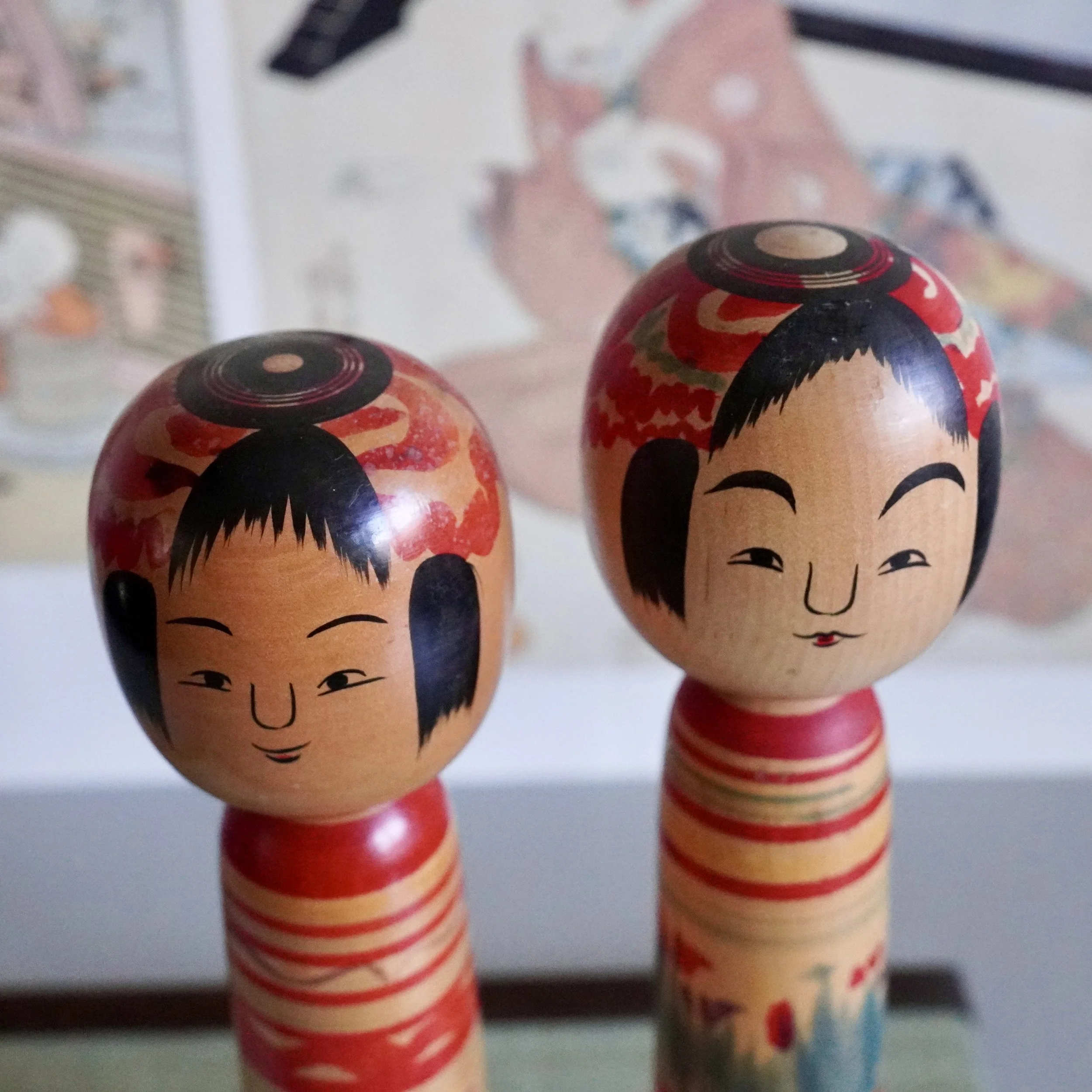 angled top view of heads of Vintage Tsuchiyu kokeshi doll pair, one face laughing open mouthed, hand painted Japanese folk art.