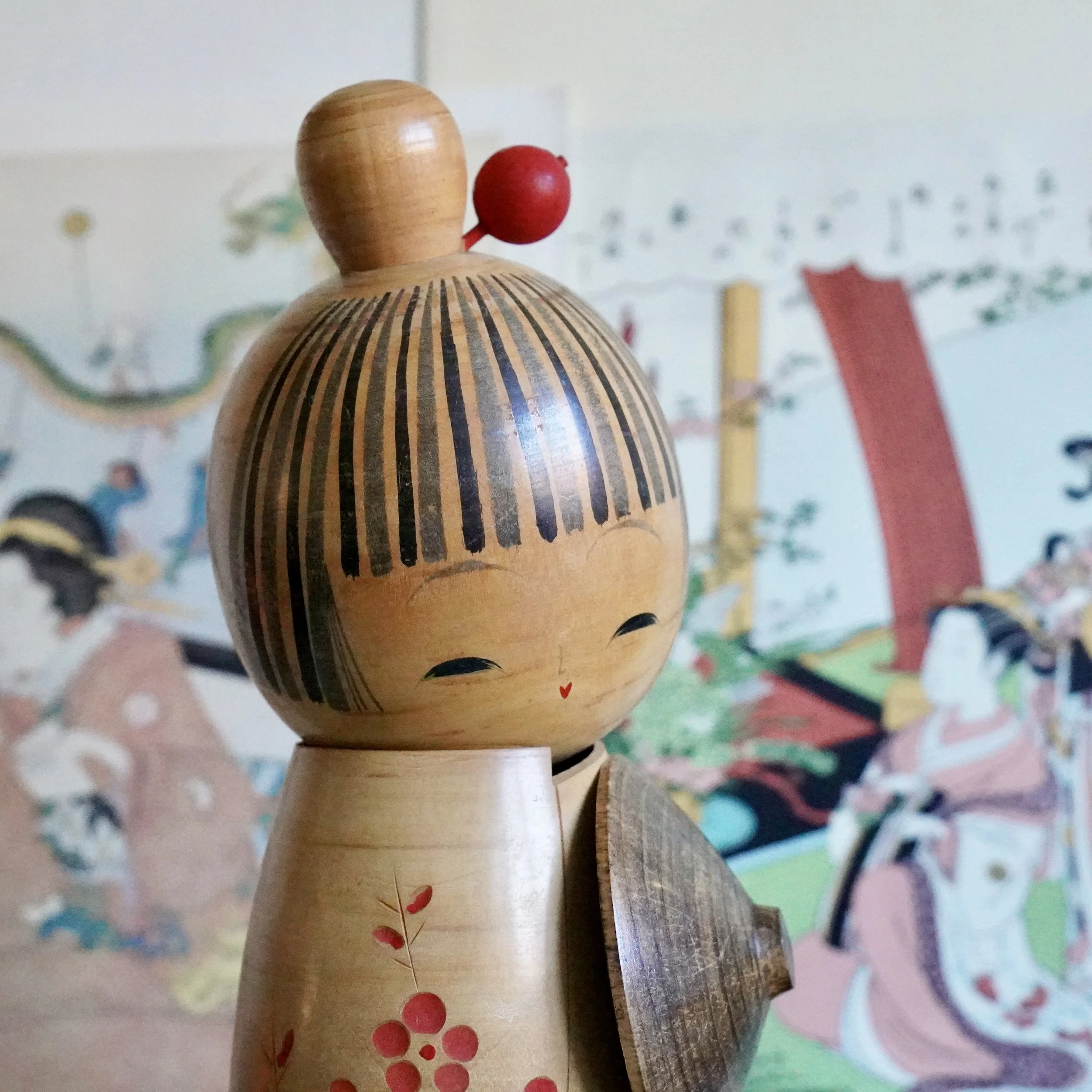 Front angle view of signed Sato Suigai kokeshi doll with red wooden hair bead ornament