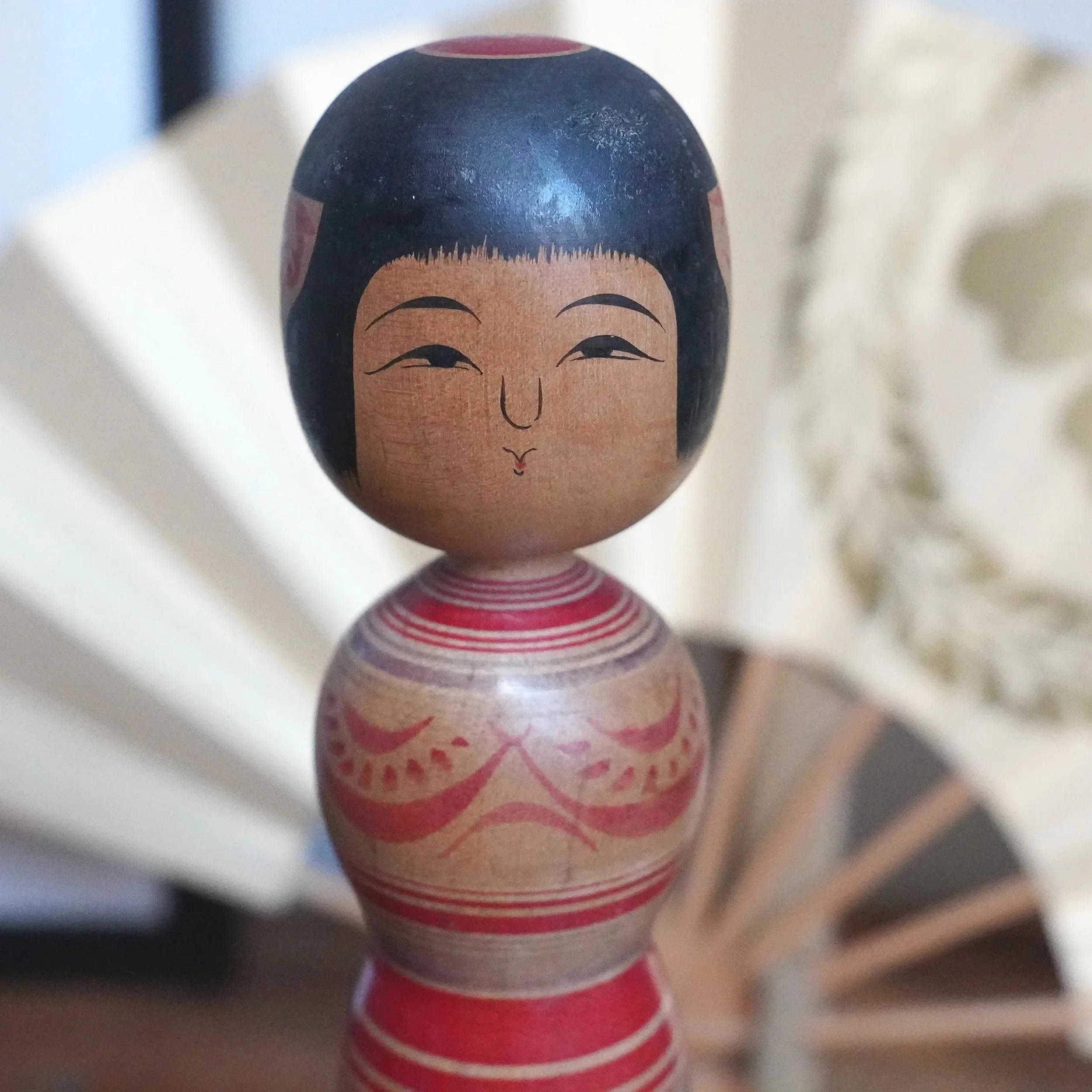 Tsugaru kokeshi doll by Sasamori Junichi, with black hair, serene face, and an hourglass body decorated with red and purple peony and stripes.