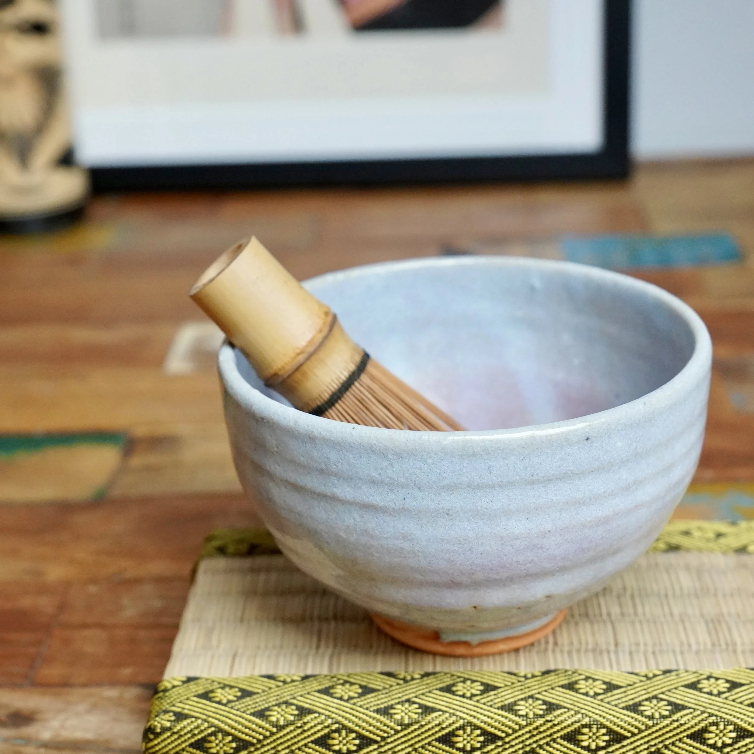 Hagi-yaki chawan, light blue-grey and lilac glaze with fine cracks, containing a bamboo whisk, on a woven mat.