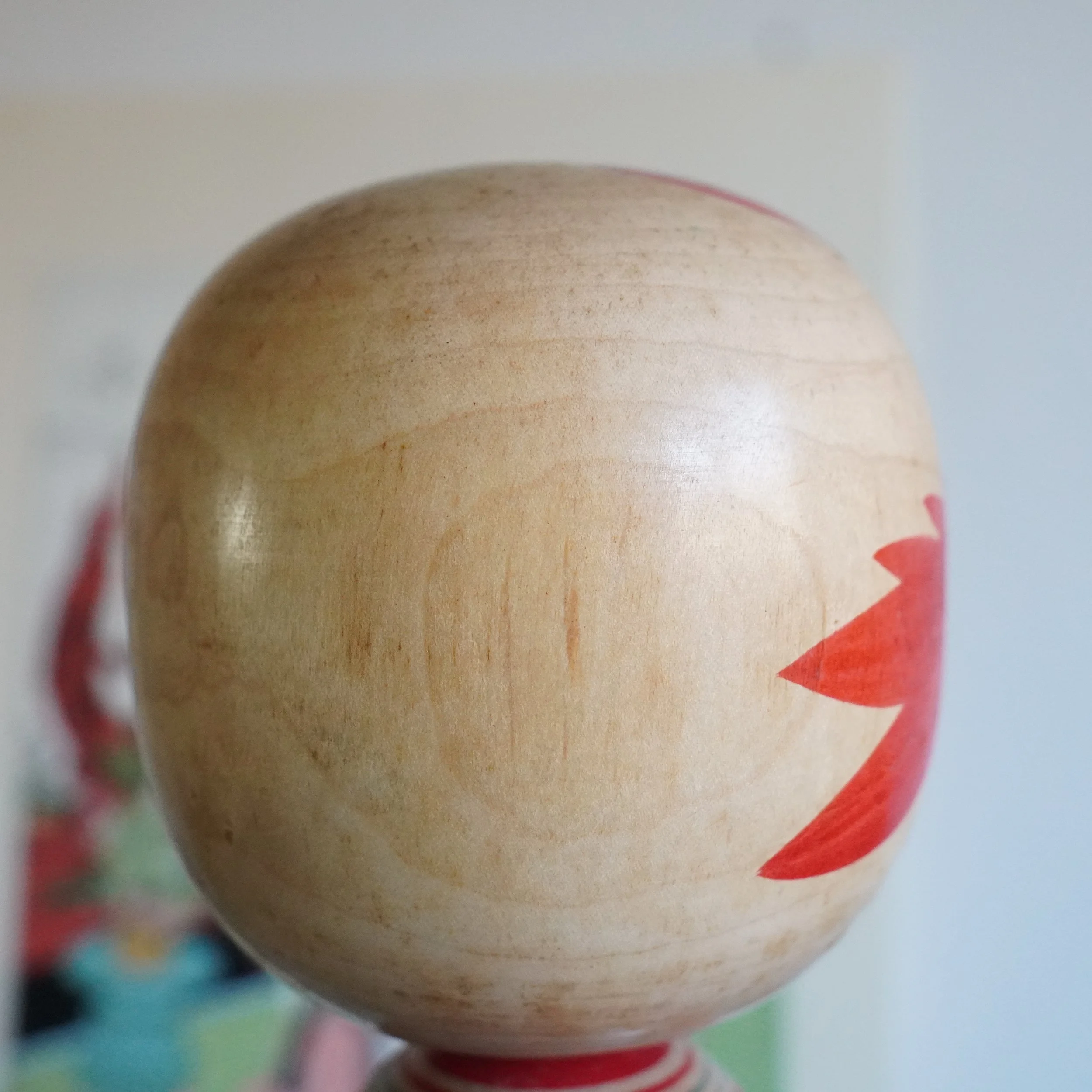 Side view of Yamagata kokeshi head by Takasaki Eiichirō showing red painted motif on smooth natural wood, rounded form, Shōwa period Japan