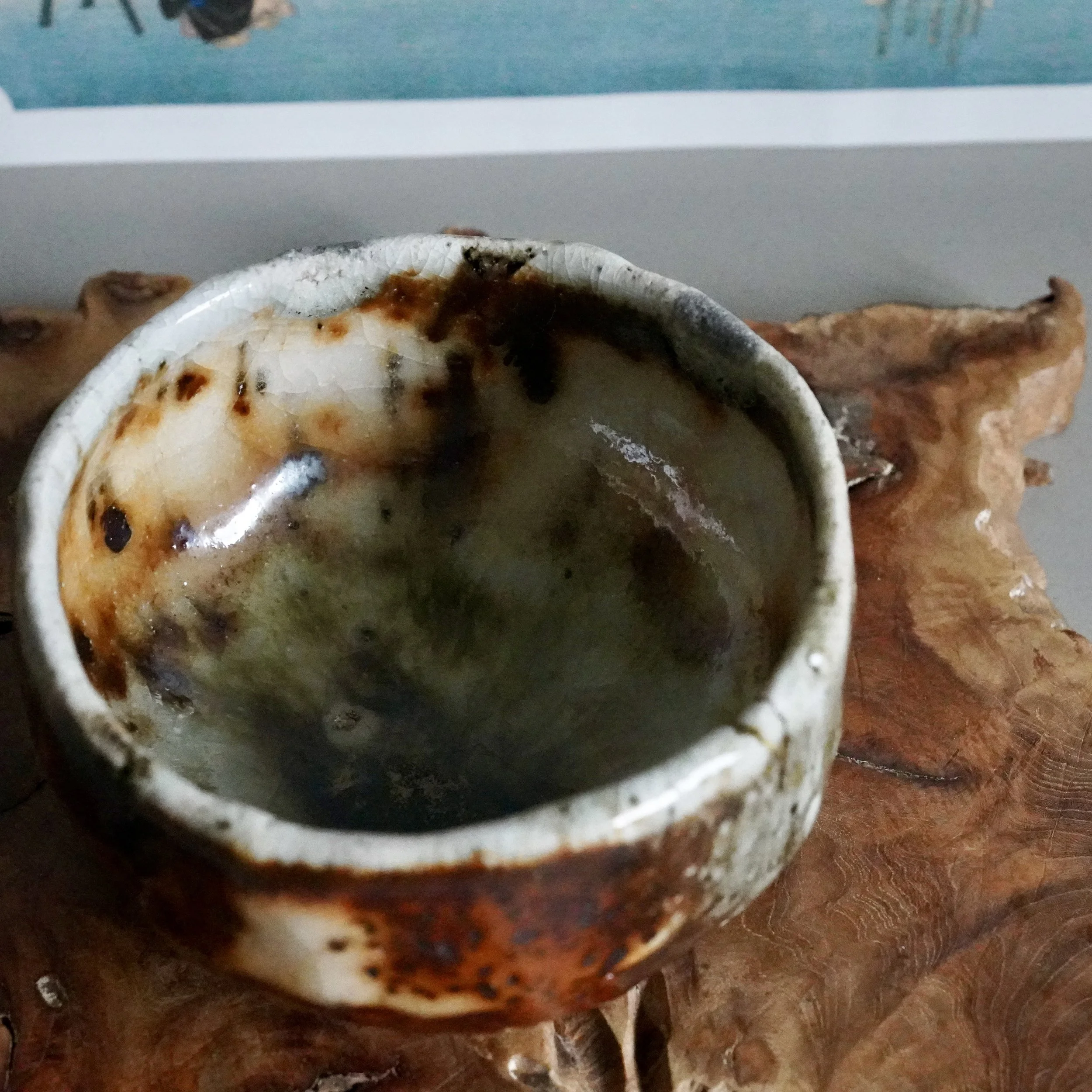 Deguchi Eiji wood-fired chawan, displaying its deep moss-green interior and crackled white, rust-brown glazed rim, on textured wood.