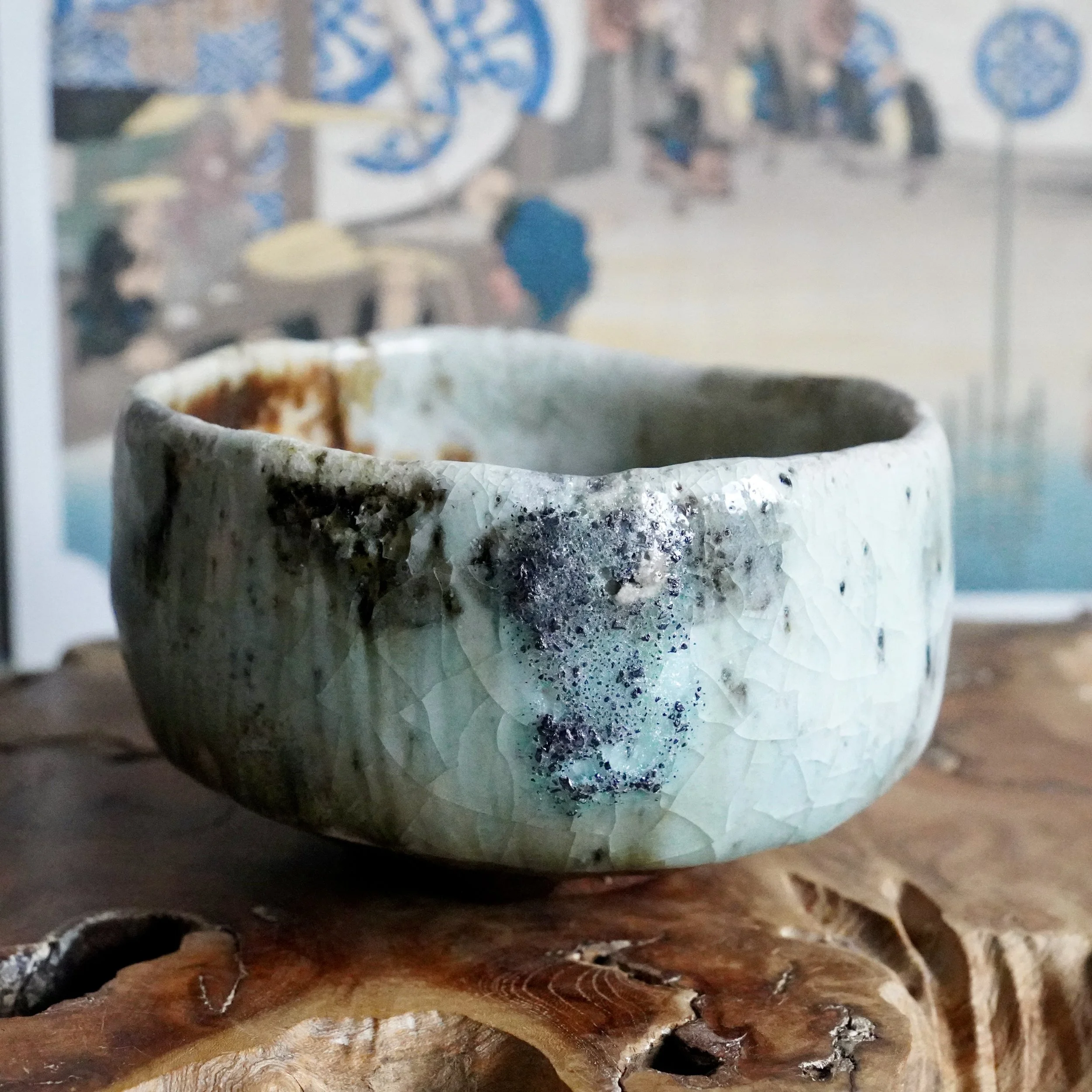 Deguchi Eiji chawan, an irregular wood-fired bowl with crackled pale blue-green glaze, dark specks, and rustic brown rim, on wood.