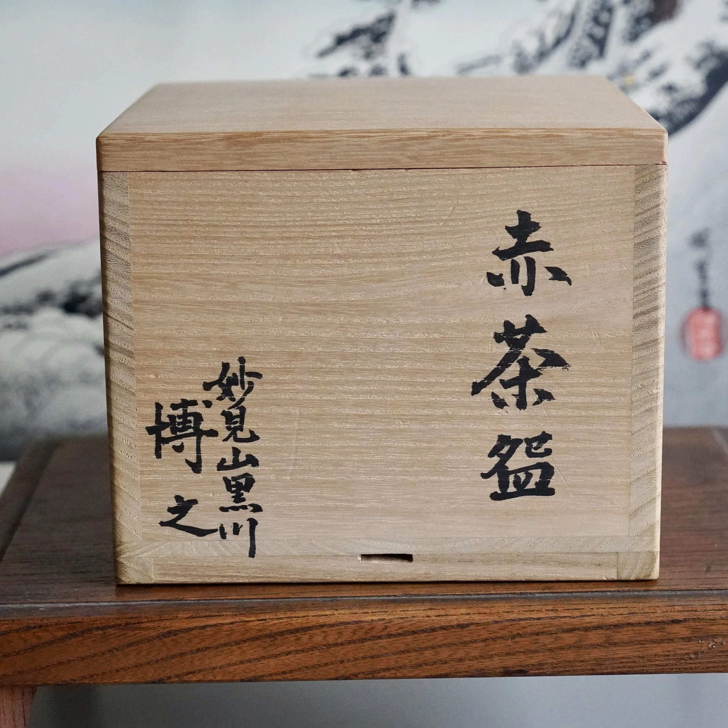 Front view of a light wooden tomobako with black Japanese calligraphy. It reads 'Aka-raku Chawan' and 'Myōkenzan Kurokawa Sawada Hiroyuki'.