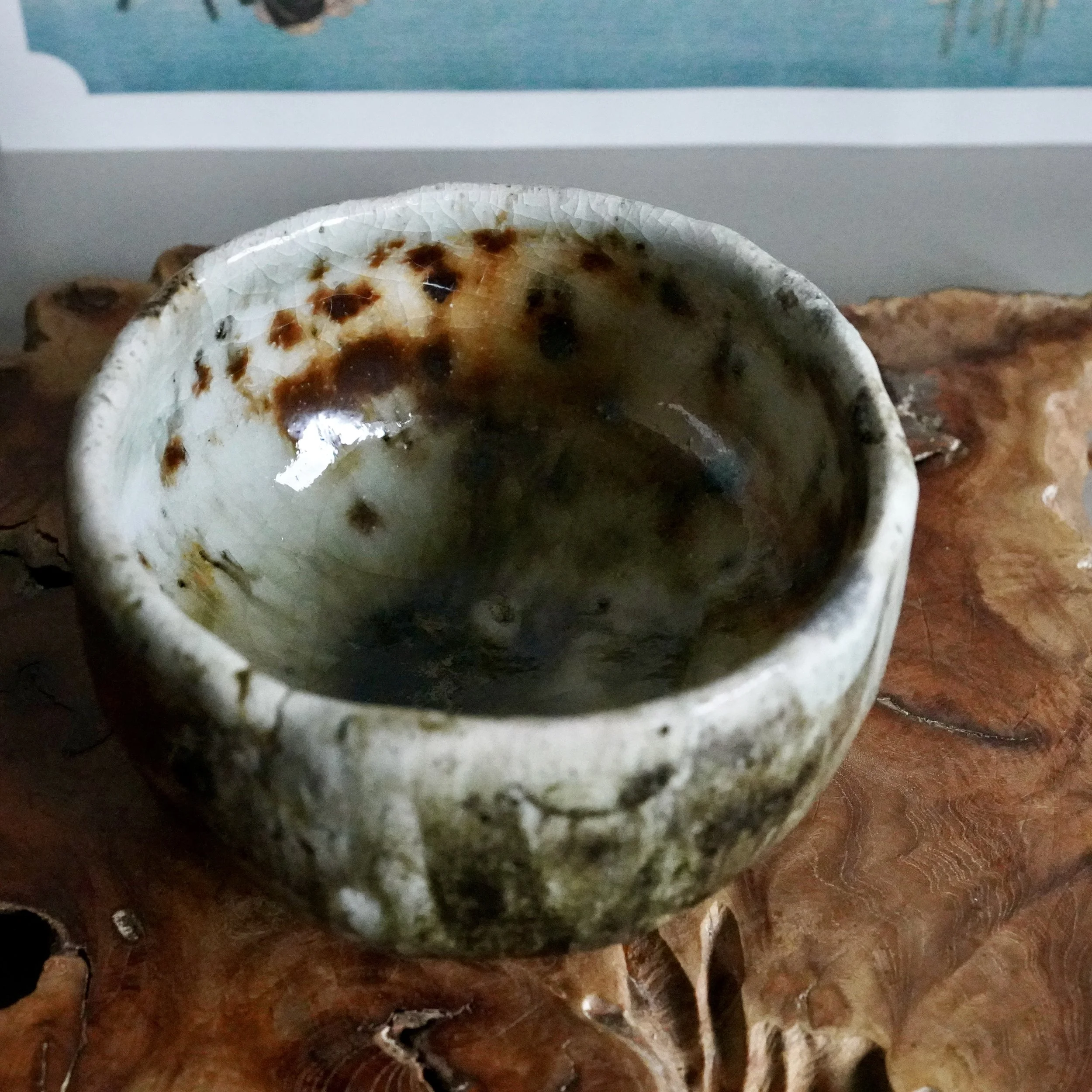 Deguchi Eiji wood-fired chawan from above, showing its crackled white, rust-brown, and dark green glaze on a textured wood surface.