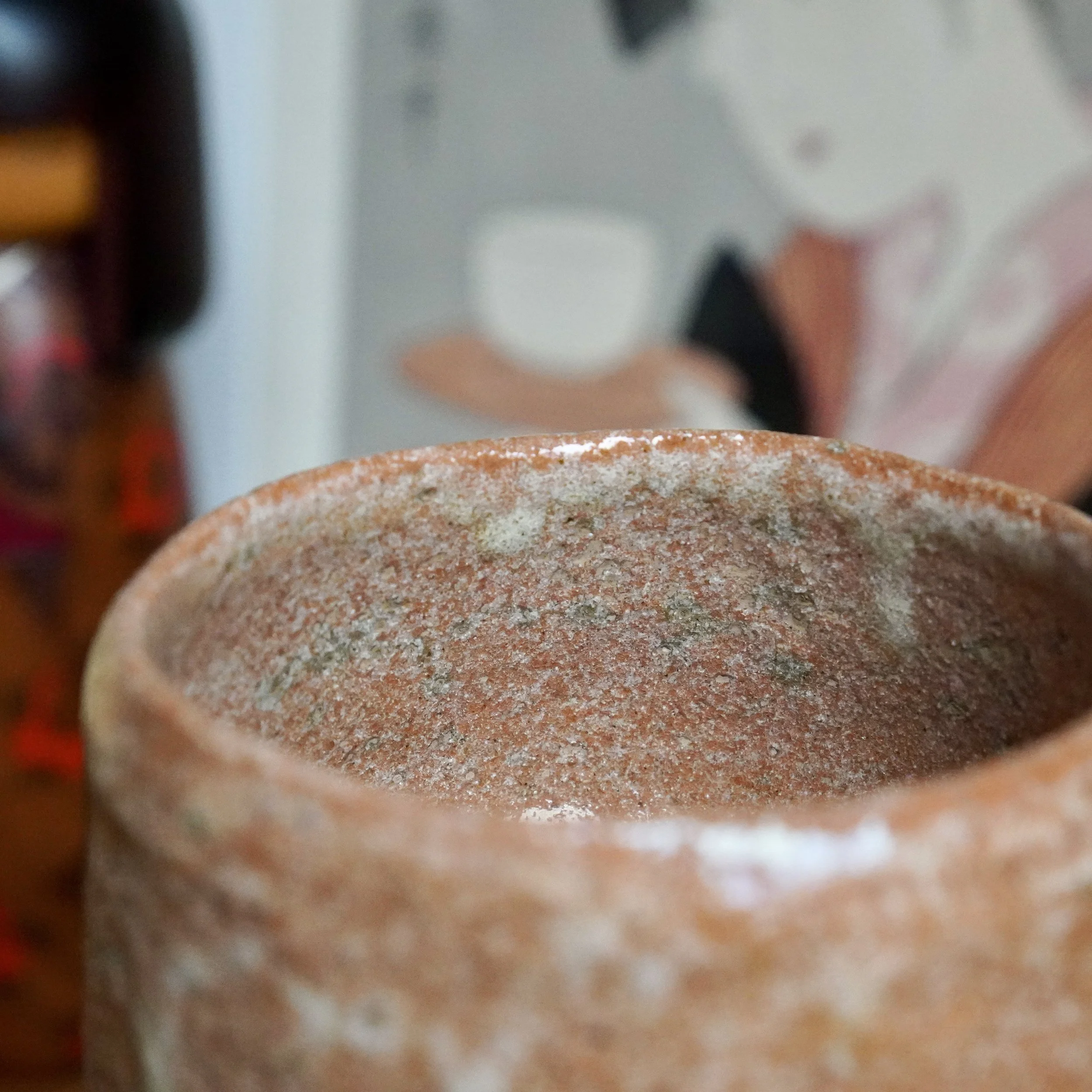 Close-up of a Sawada Hiroyuki aka-raku chawan interior, showing rugged, pitted, reddish-orange clay and a prominent white glaze drip.