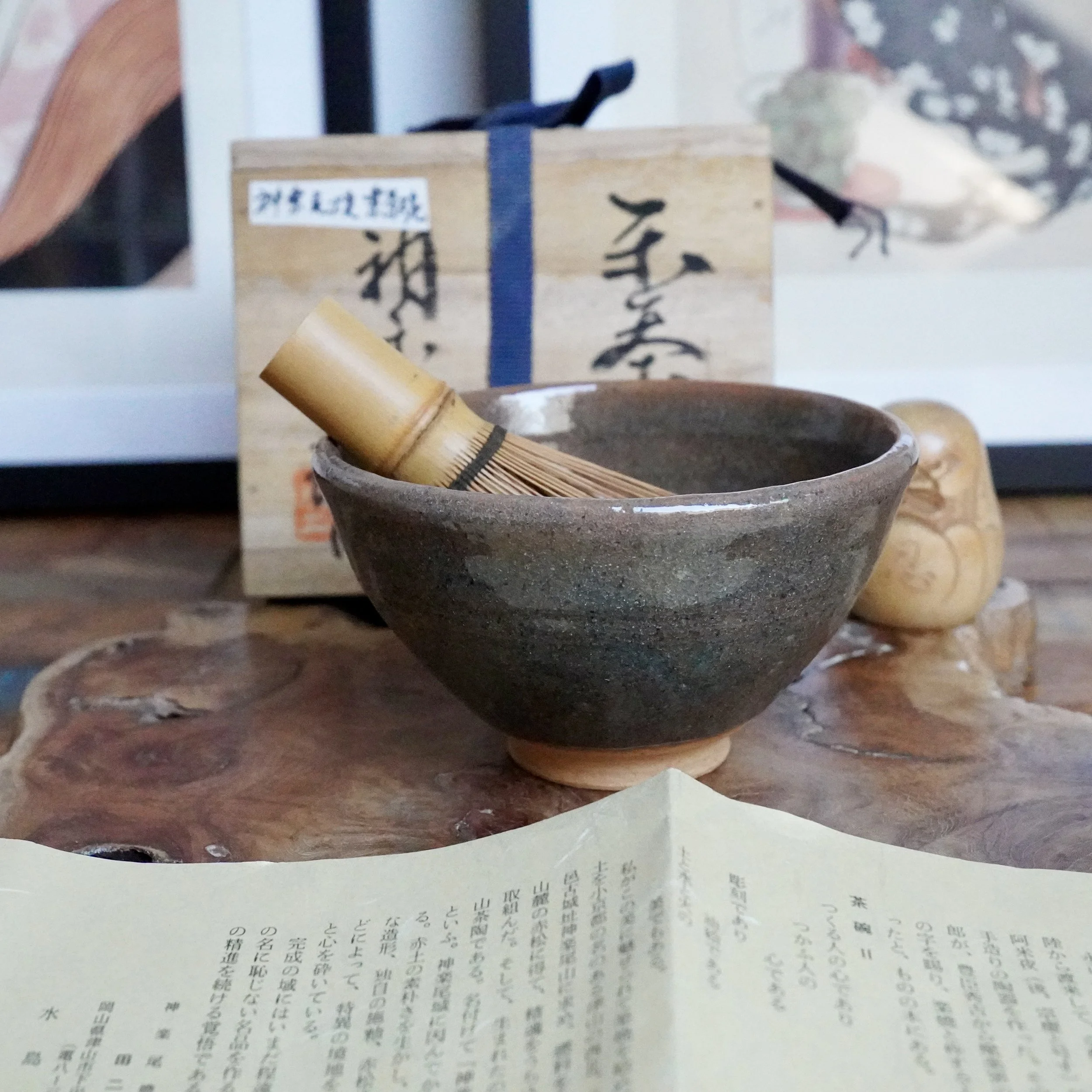Mizushima Jirō Kagurao-yaki chawan, dark with a coarse textured glaze, holding a bamboo whisk, placed with its wooden box and shiori paper.