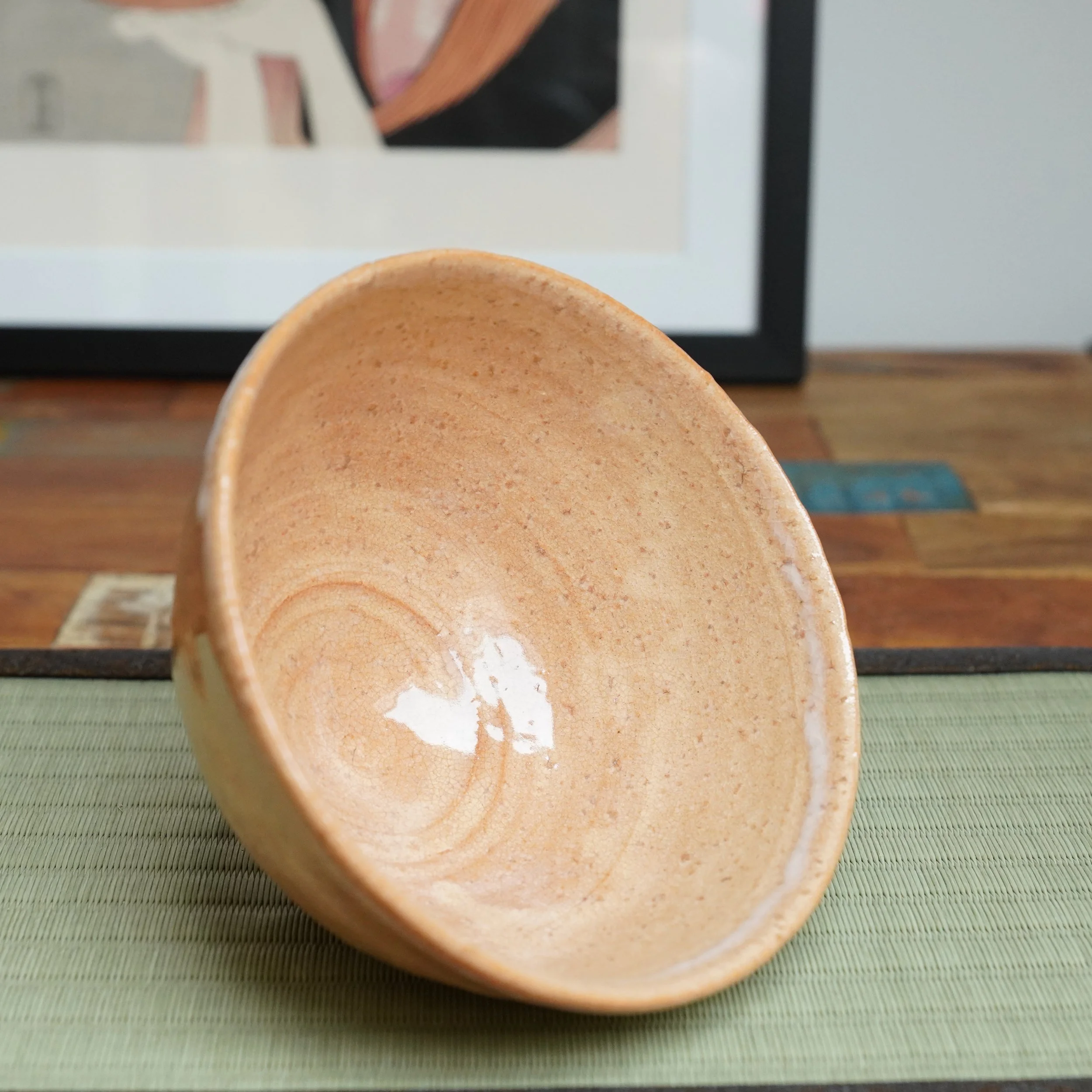 Tilted Hagi-yaki chawan by Kaneko Nobuhiko, showing its speckled salmon pink interior with milky white glaze and crackle, resting on a tatami mat.