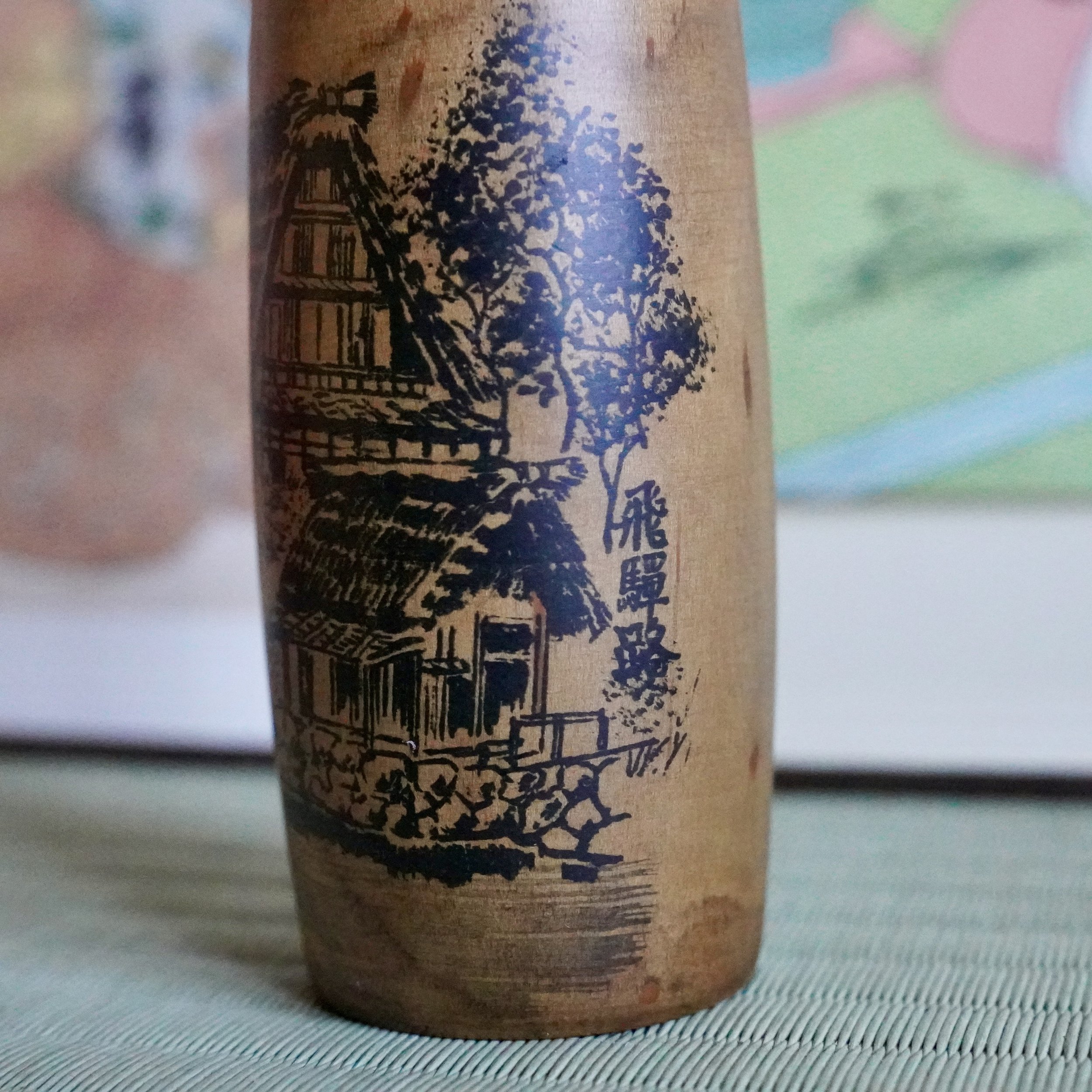 Close up of painted thatched Hida farmhouse and pine trees, Usaburō kokeshi doll