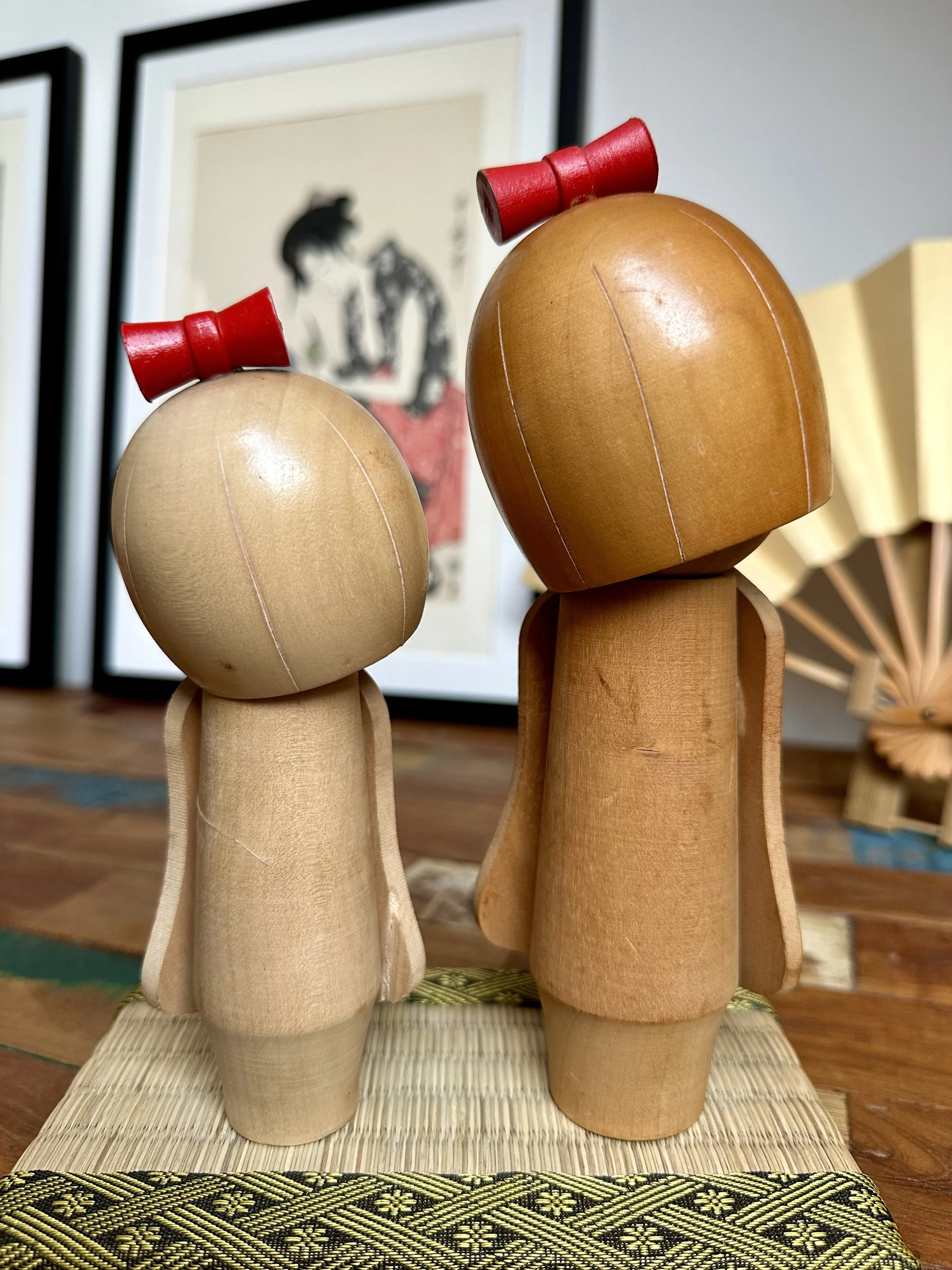 Back view folding panel kokeshi plain wood reverse both pieces red bow visible gold fan background