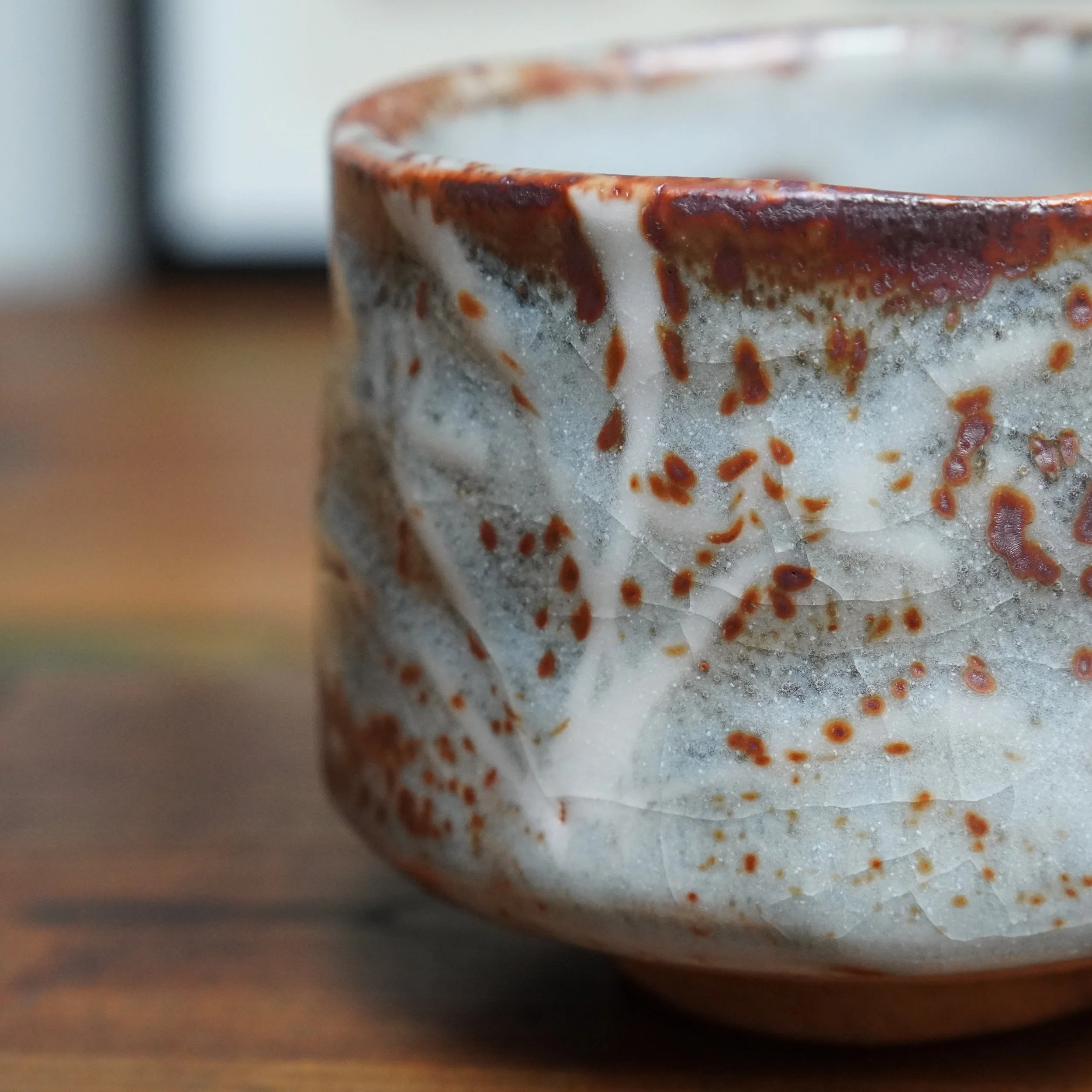 Close-up side view of a chawan, white-grey glaze with red speckles and fine crackle texture. A darker reddish rim is visible.