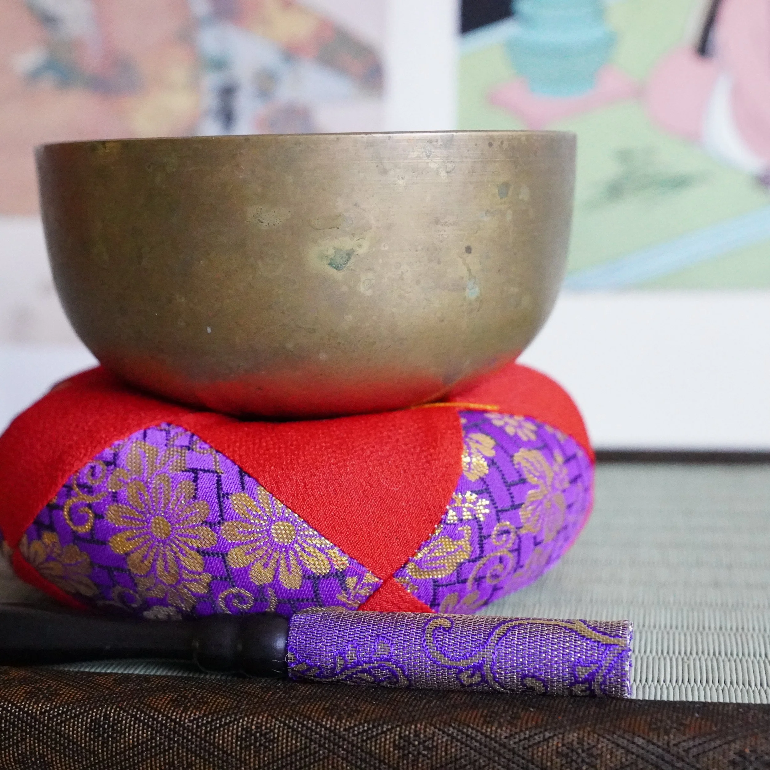 Front view of bronze orin bowl on brocade cushion with wooden striker, tatami mat