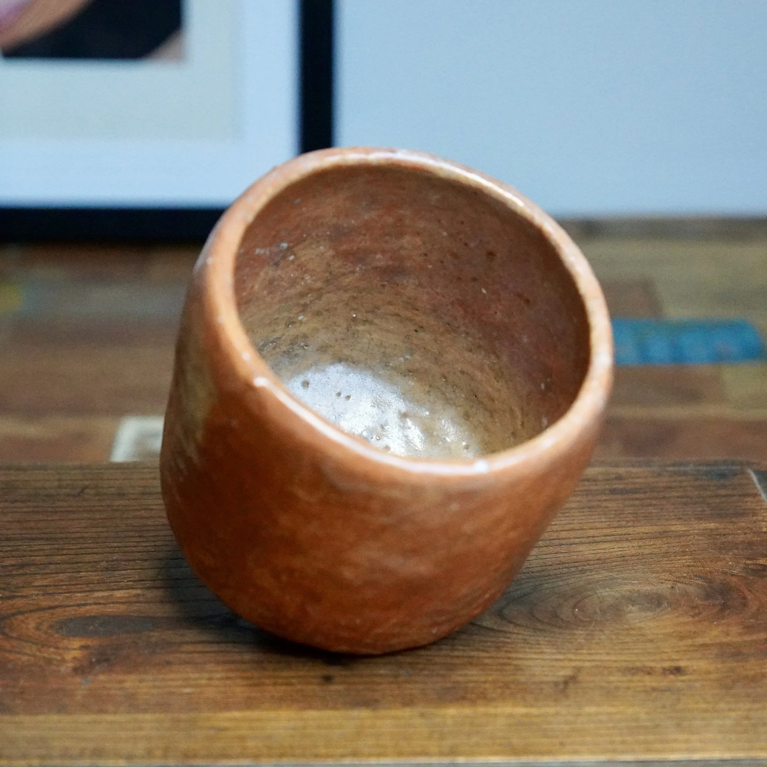 Angled reddish-brown ceramic tsutsu chawan by Hioki Nanshū kiln, showing its textured interior with light marks, on a dark wooden surface.