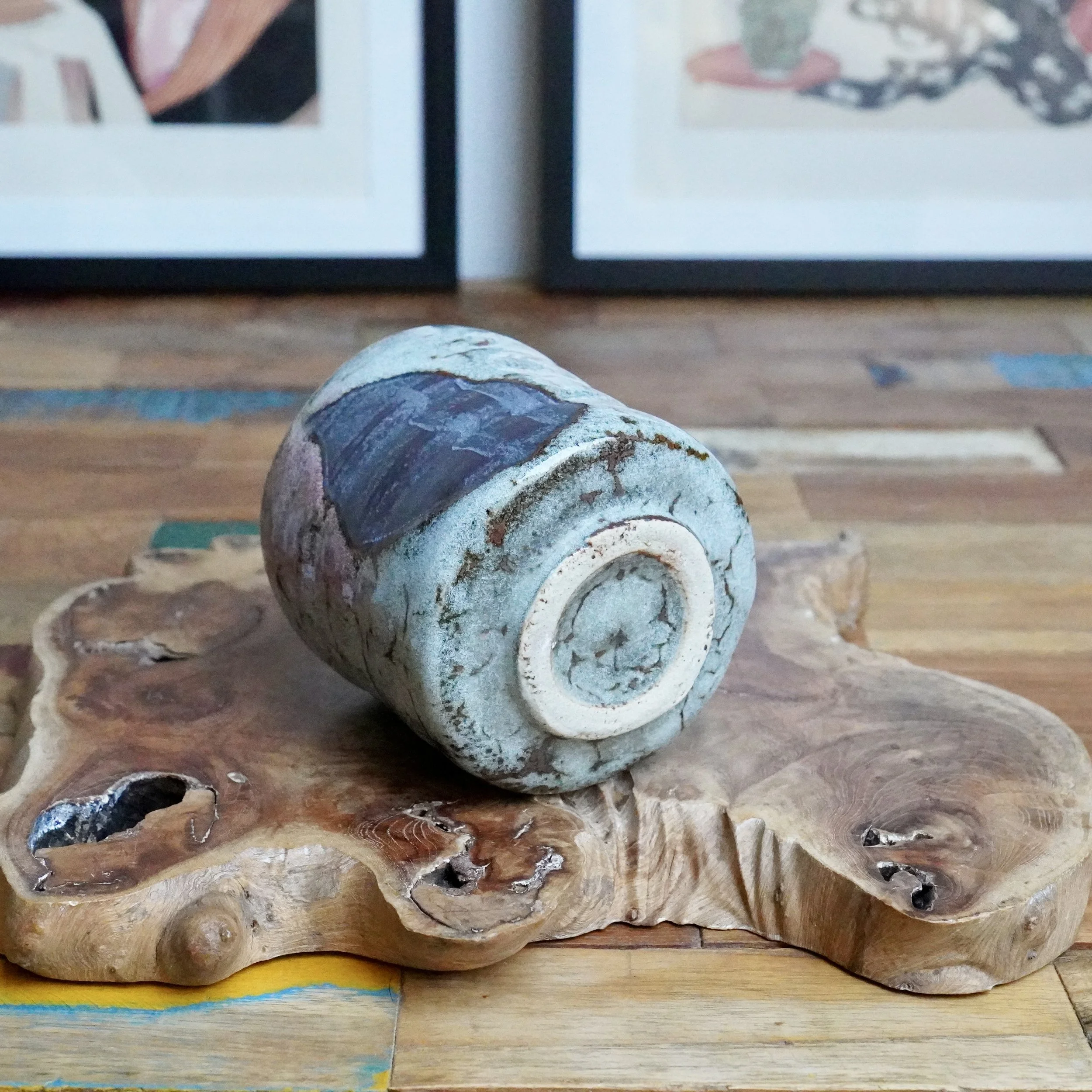 Chawan by Tsuchiya Issui, on side, displays layered turquoise and grey glaze with brown lines, on an organic wood slab and multicolor table.