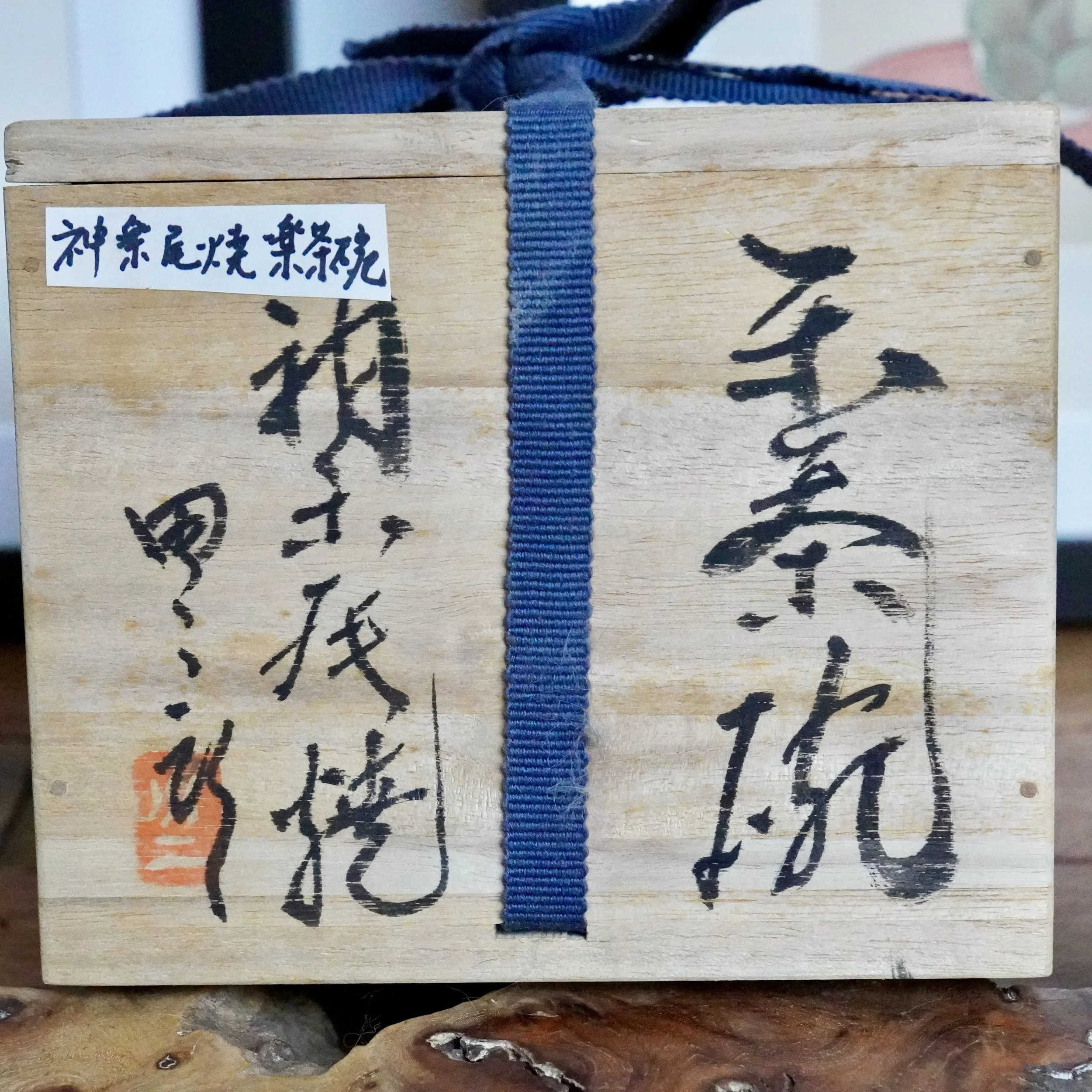 Wooden tomobako for a Kagurao-yaki chawan, secured with a blue ribbon. Black calligraphy identifies it as a Raku teabowl by Mizushima Jirō, with a red seal.