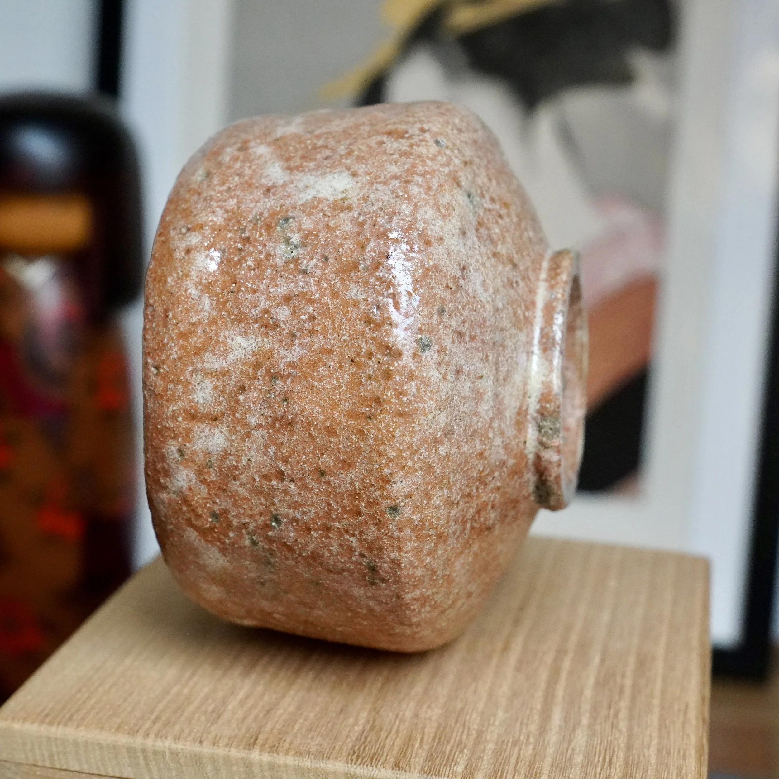 Aka-raku chawan by Sawada Hiroyuki, a textured reddish-orange bowl with a distinctive pale white glaze drip and rough surface, resting on wood.