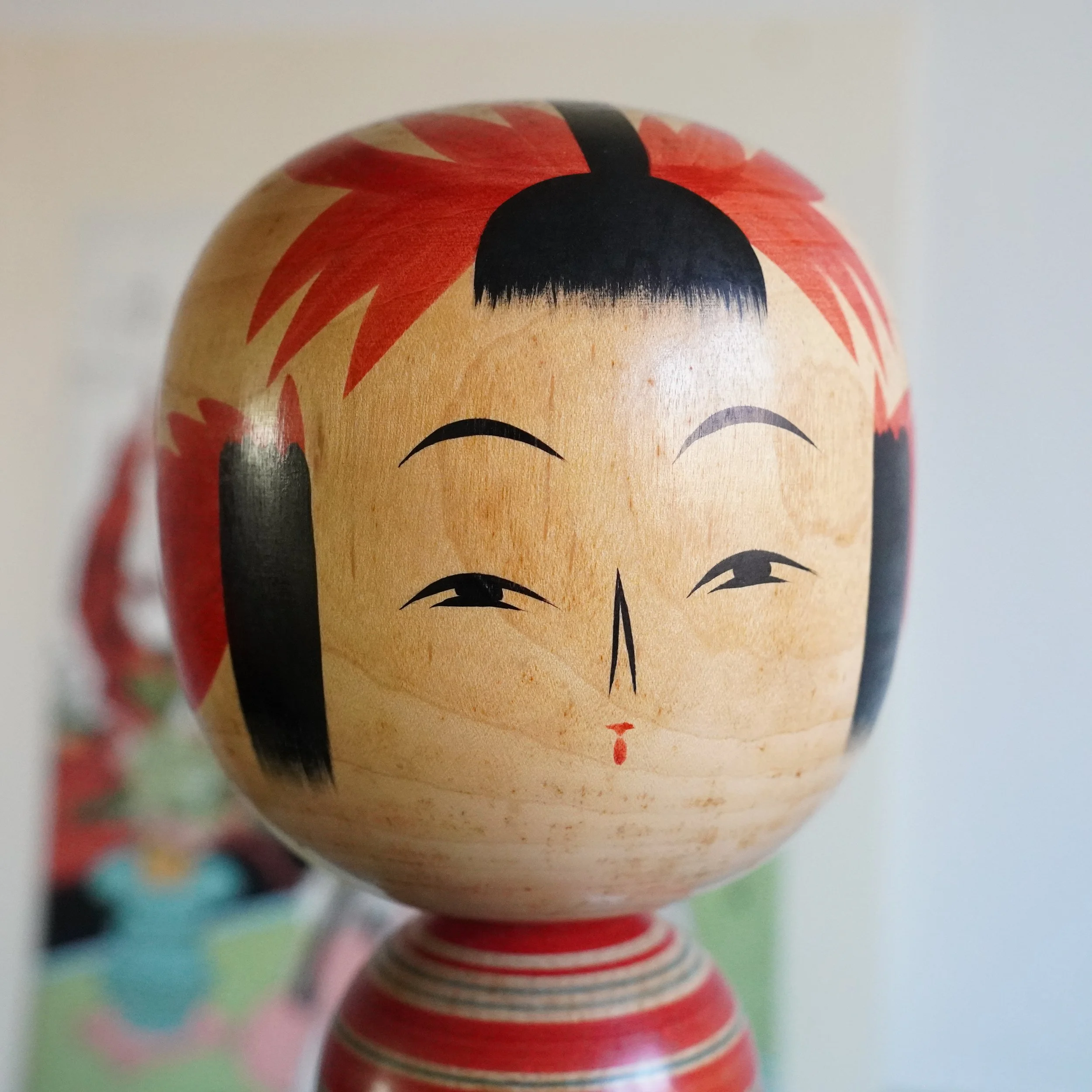 Yamagata kokeshi face close-up by Takasaki Eiichirō, painted facial features, red floral hair decoration, black eyebrow lines, small red mouth, smooth natural wood, Shōwa period