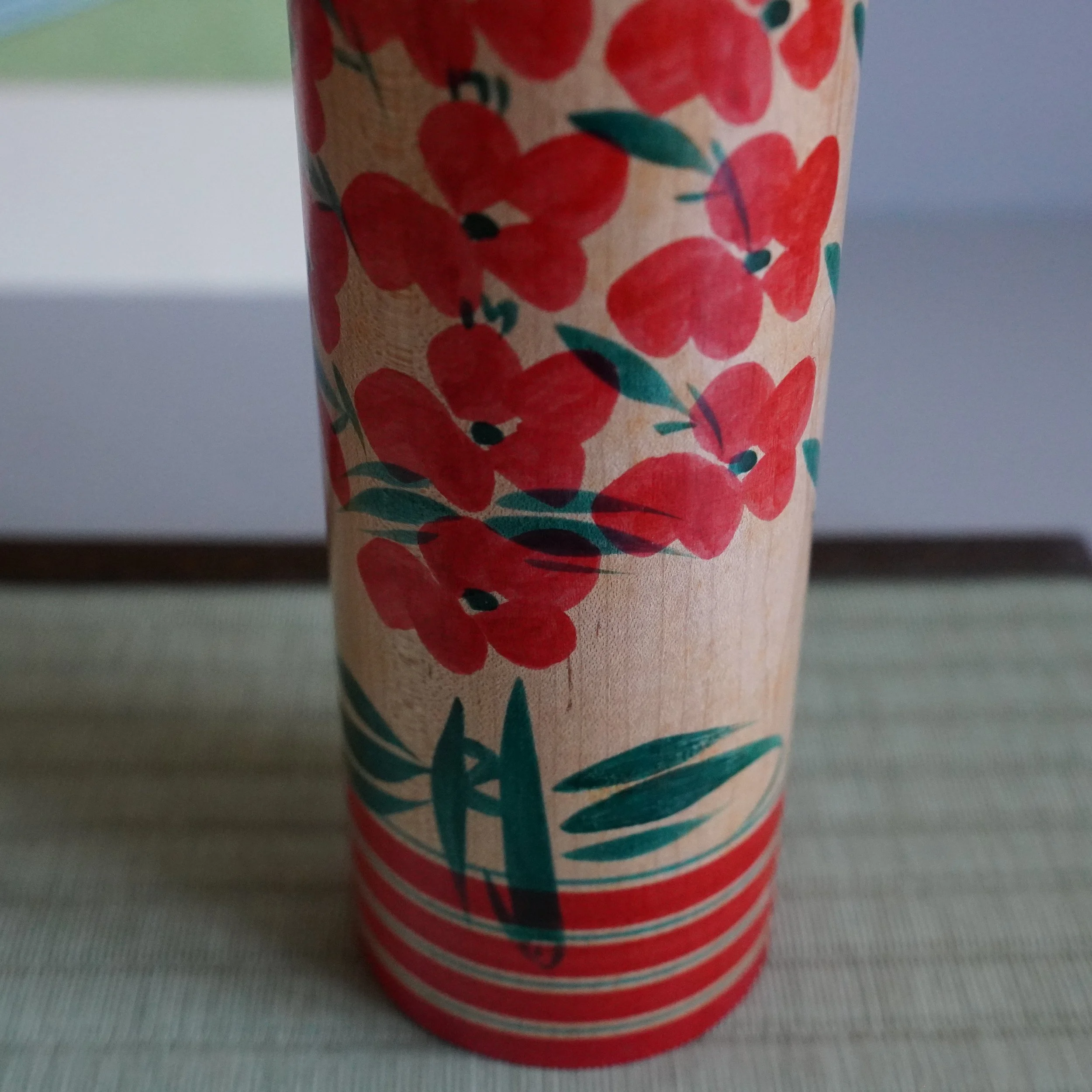 Body decoration detail of Yamagata kokeshi by Takasaki Eiichirō, hand-painted chrysanthemum motif in soft red with green leaf accents on natural wood, Shōwa period Japan