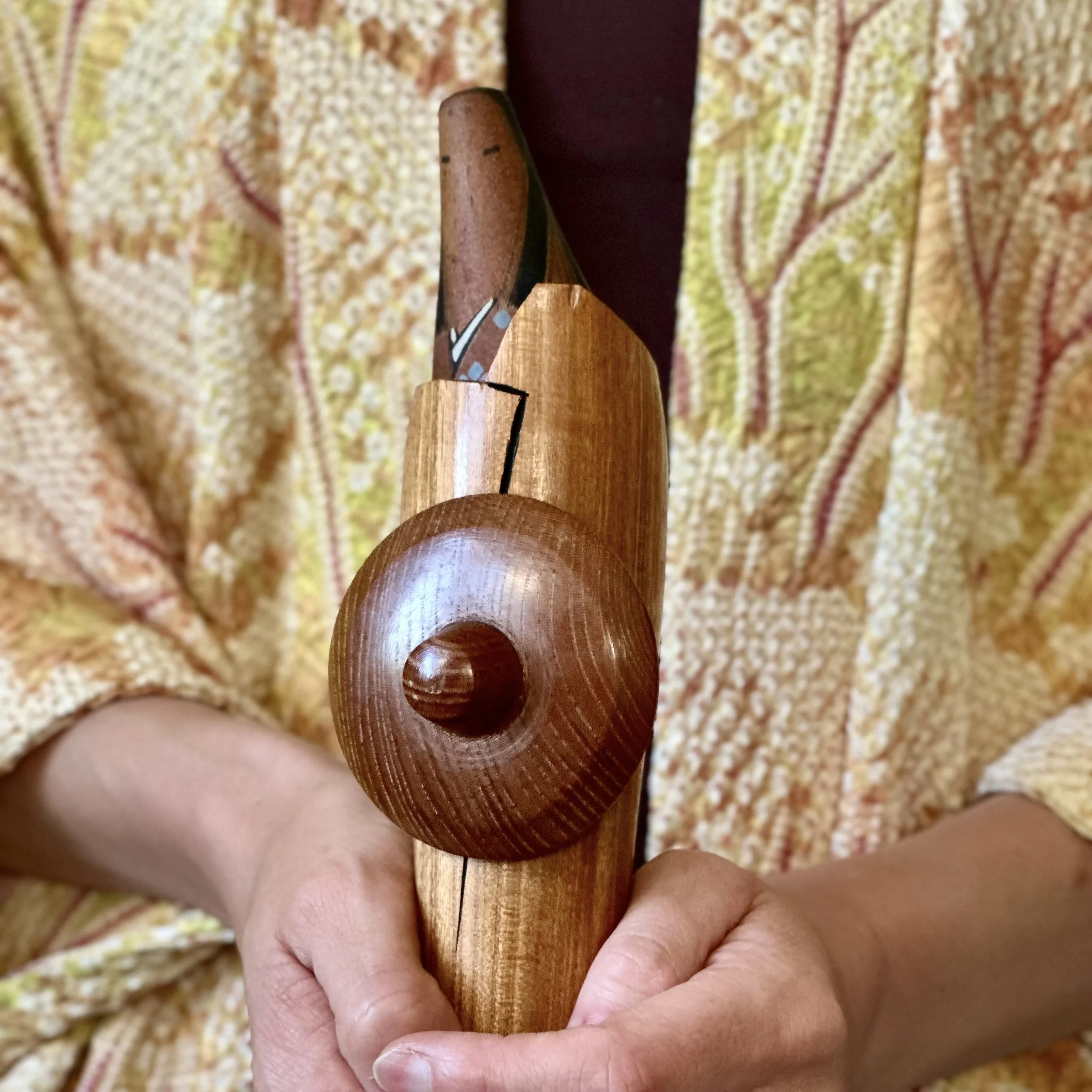 Close up of the wooden kasa travel hat on a sōsaku kokeshi by Sato Suigai, held in the hand to show the dowel join and carved plum blossom decoration on the body, Shōwa period