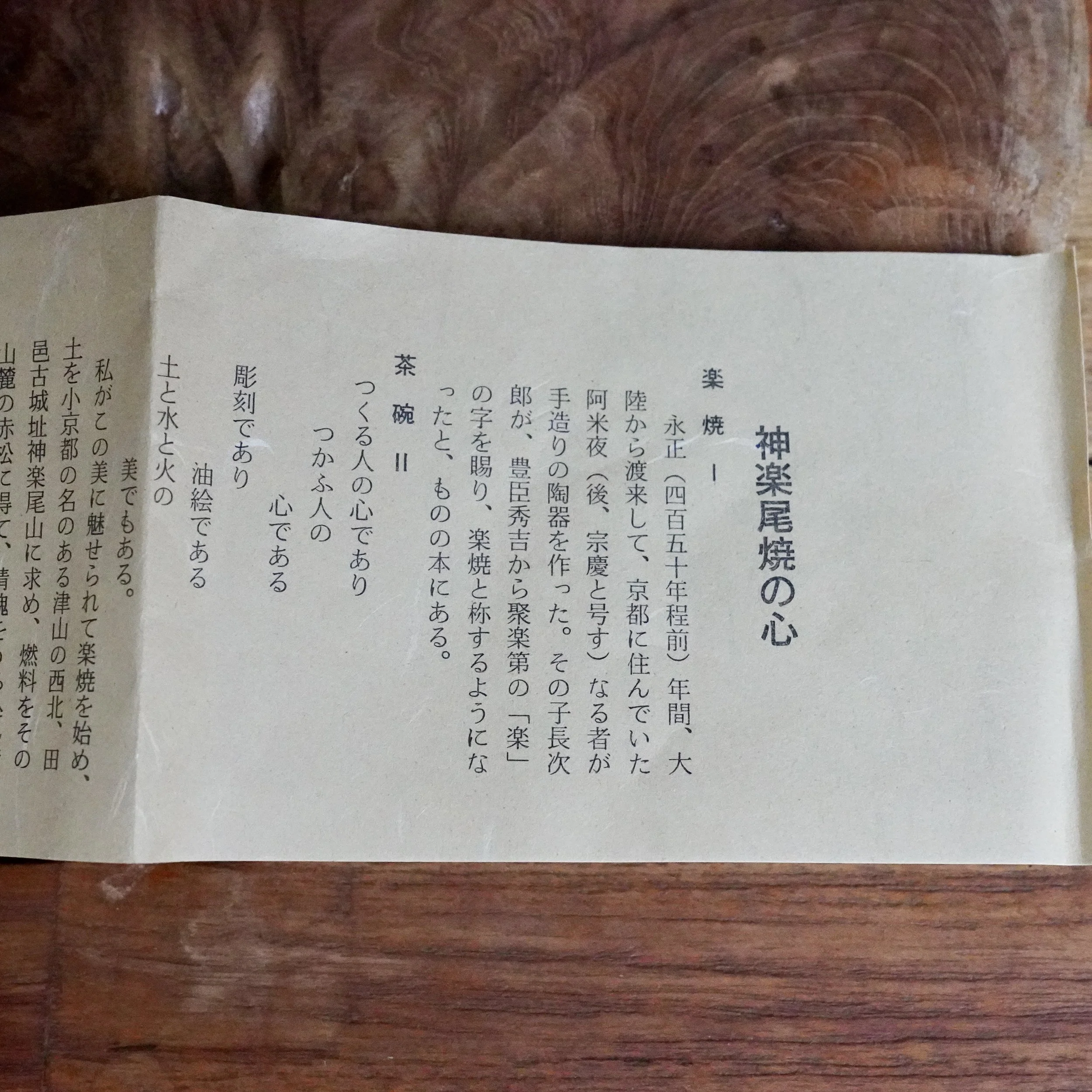 Mizushima Jirō's handwritten shiori on textured, off-white paper, featuring dense vertical Japanese text, resting on a dark wood surface.
