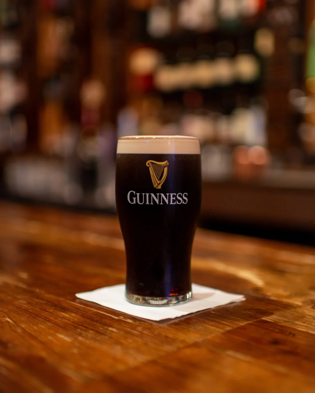 A pint of Guinness beer on a wooden bar counter with a blurred bar background.