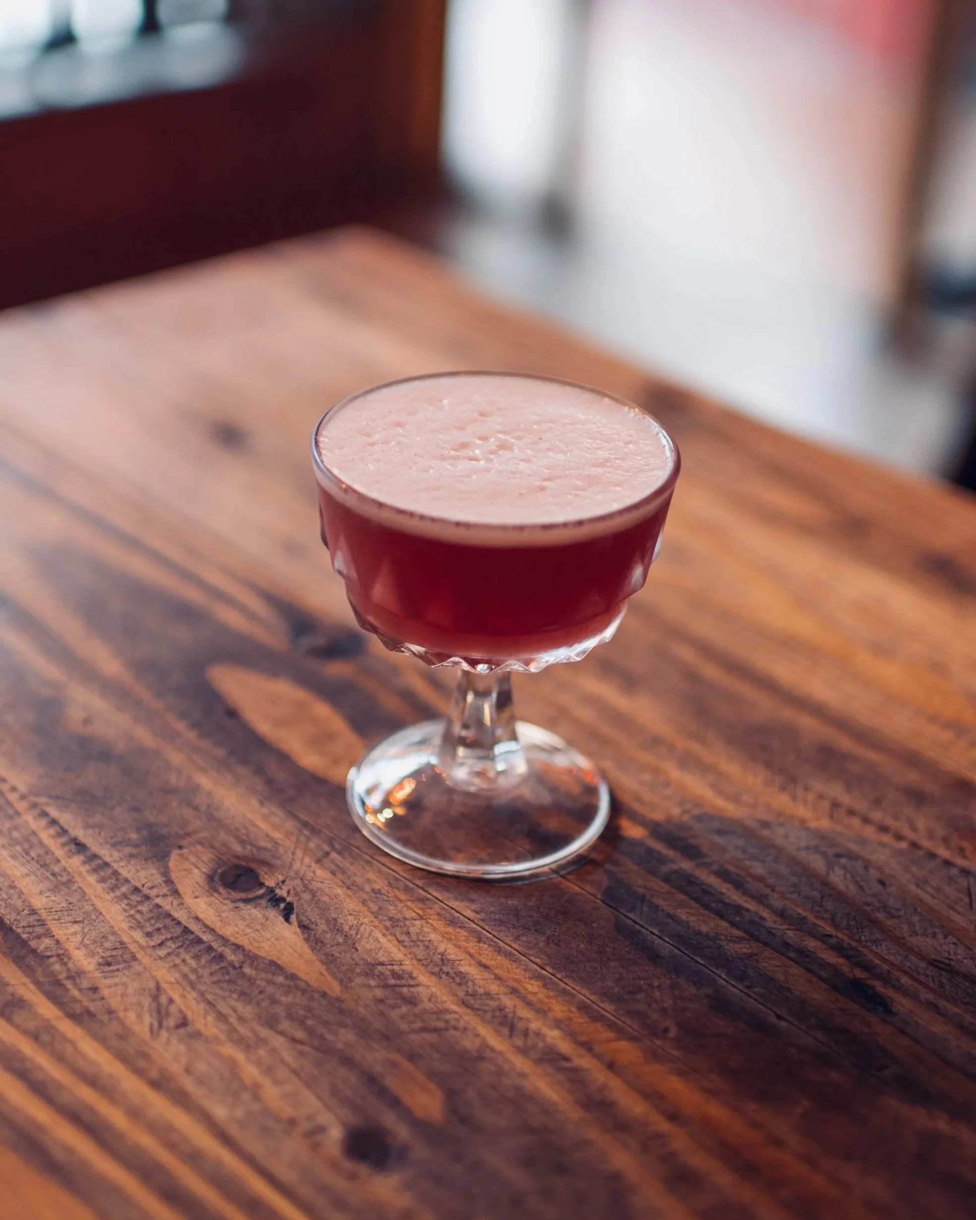 A cocktail in a stemmed glass with a wide, rounded bowl and a flat base on a wooden table.