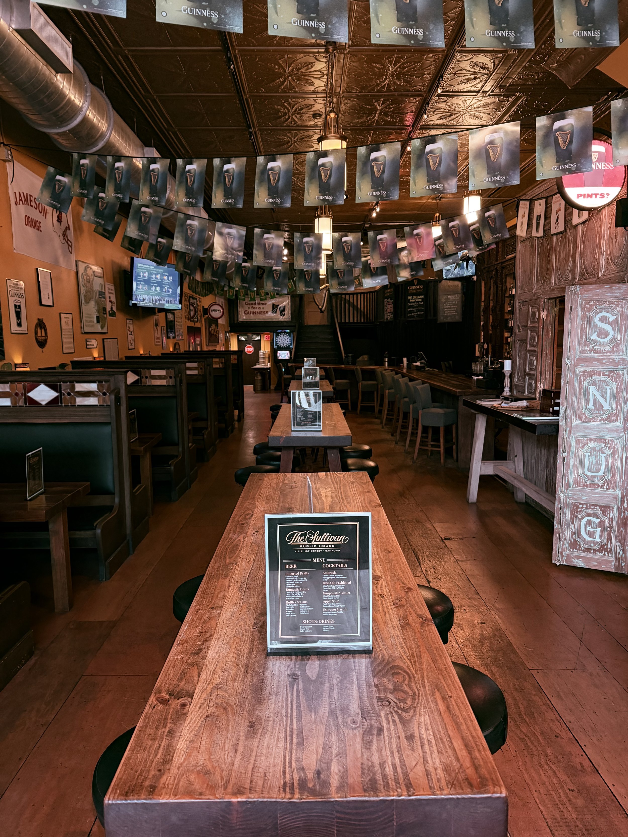 Empty bar and dining area in a pub decorated with Guinness banners and signs, with wooden tables and chairs.