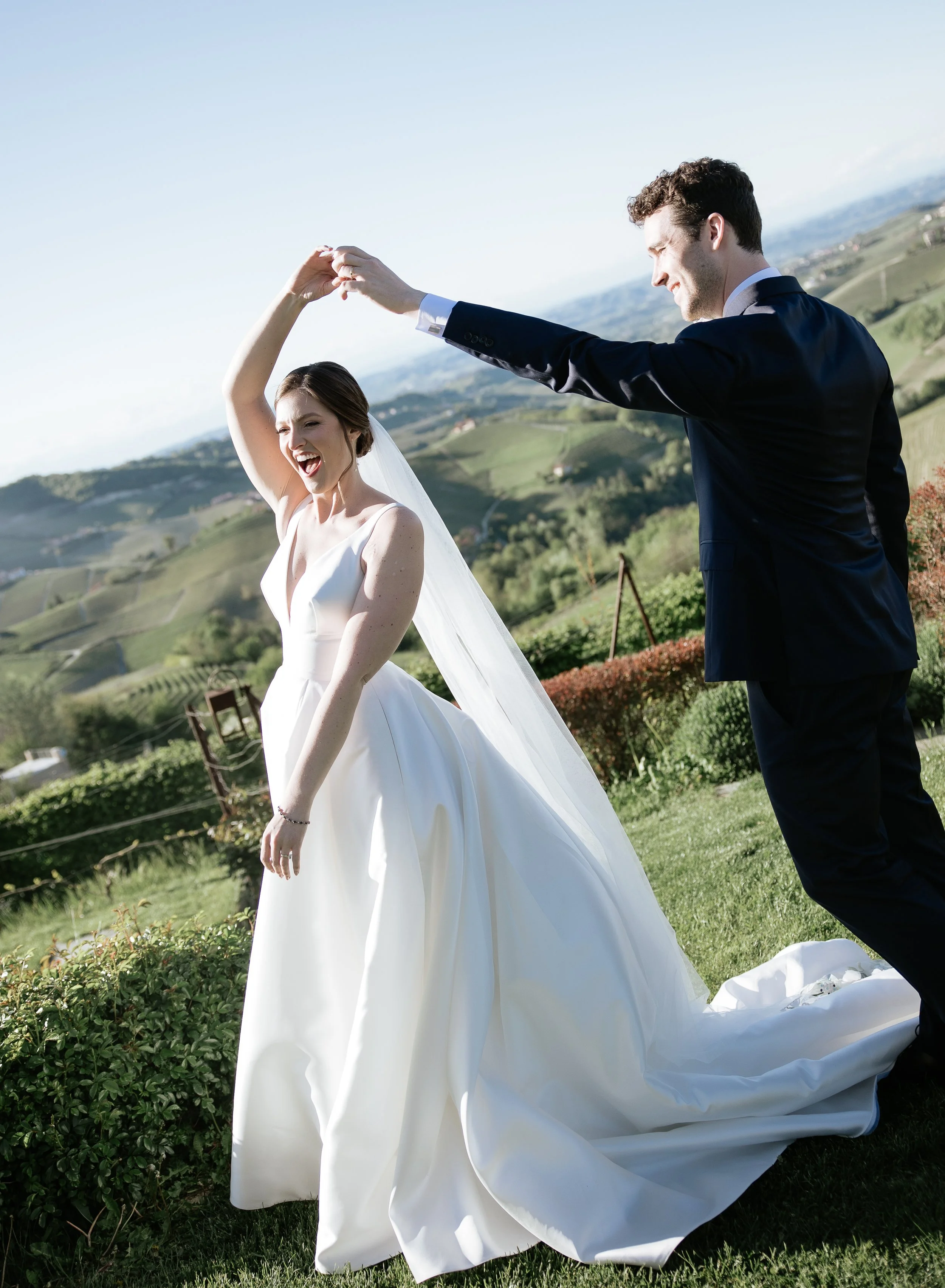 Una coppia di sposi balla all'aperto, con un paesaggio di colline verdi sullo sfondo, durante un matrimonio.