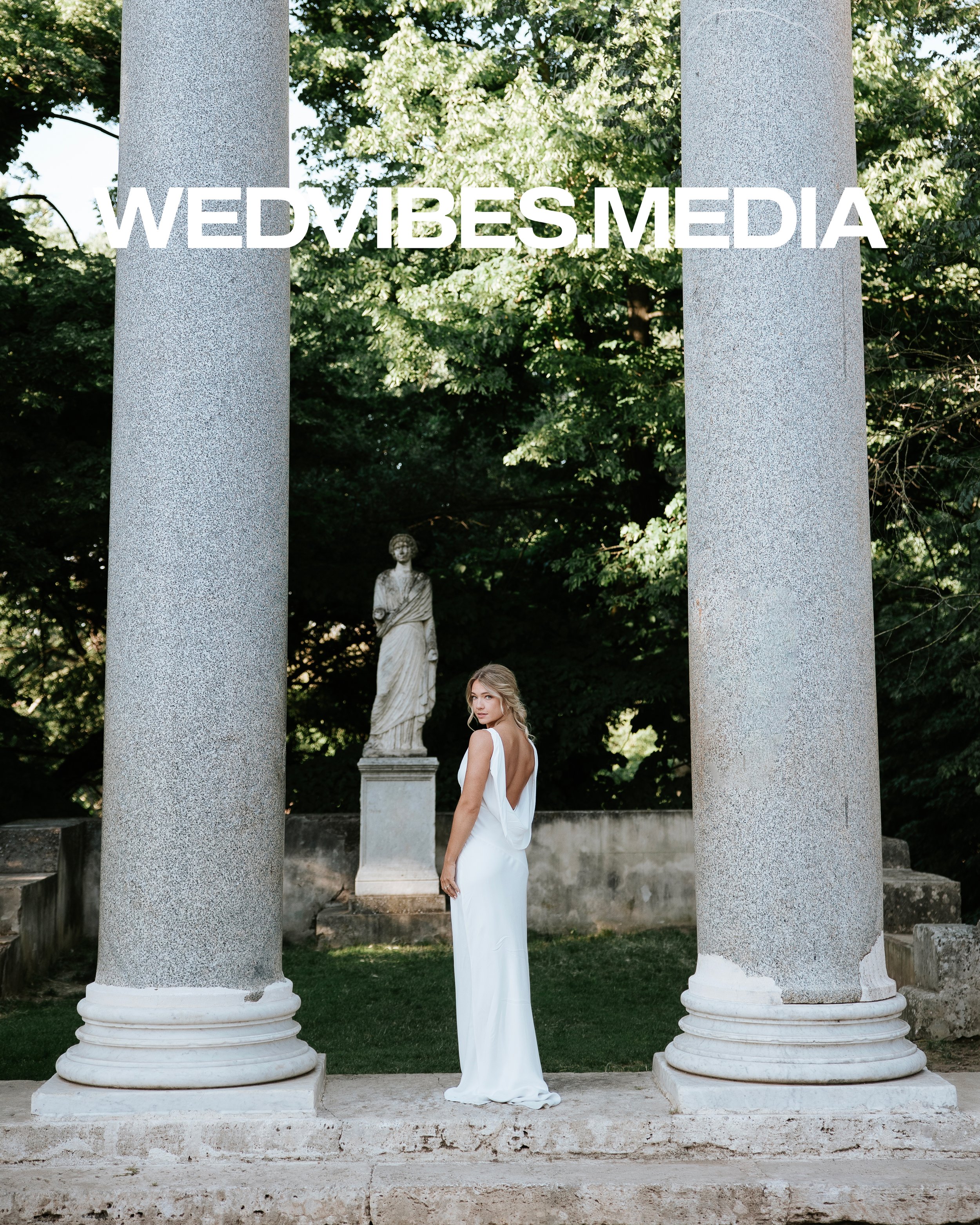 Bride during an elopement at Villa Borghese, Rome. Imperial dress. She stays in the middle of two columns. The place is green and elegant. She is blonde.