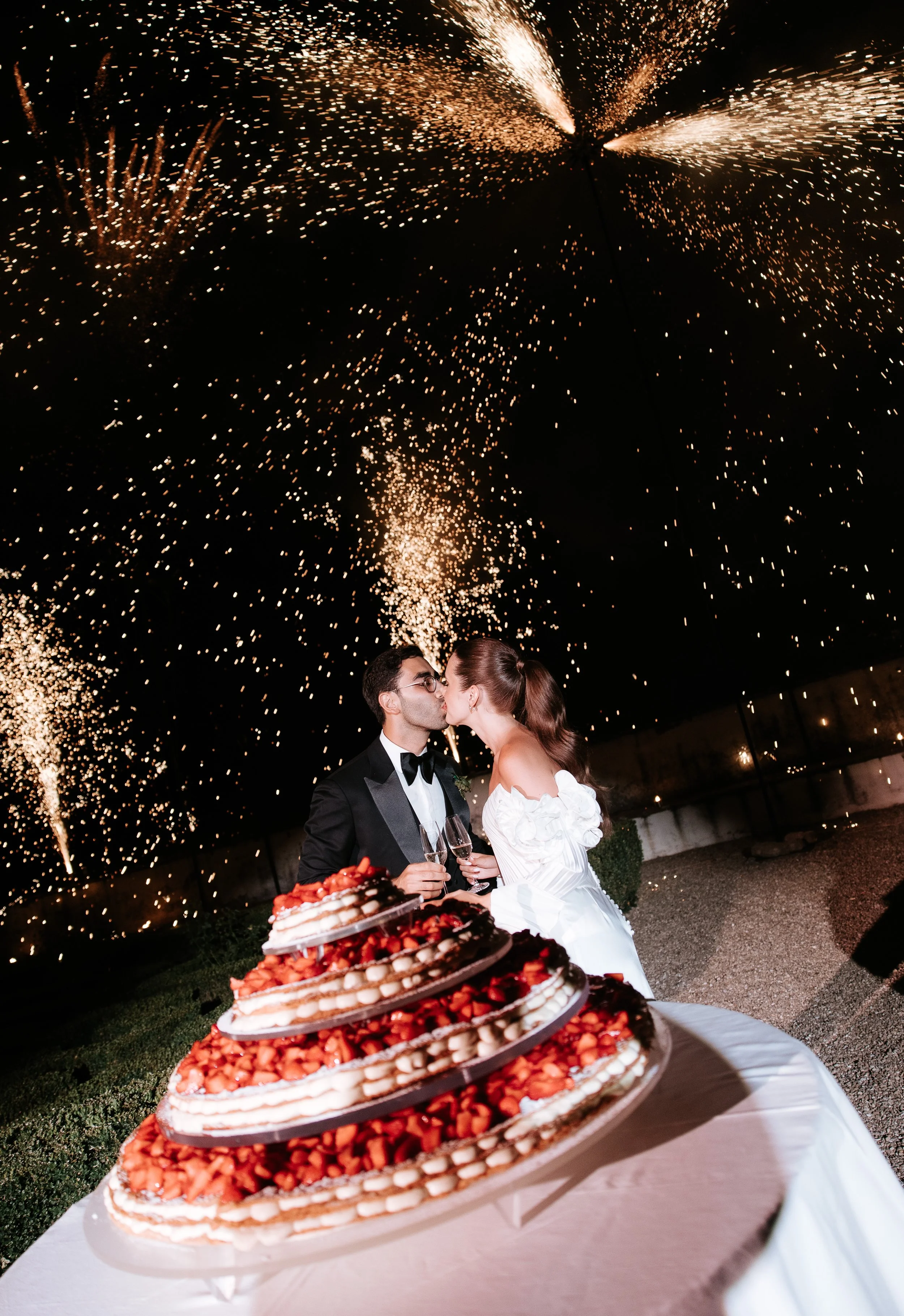 couple kiss after the cake cut and during fireworks at villa corsini a mezzomonte, wedding in italy, red cake