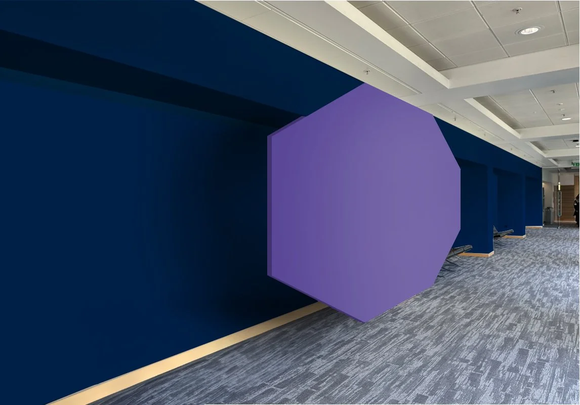 Interior of a modern building with a navy wall and a large purple octagonal sculpture protruding from the wall, with benches along the wall and a gray patterned carpet.