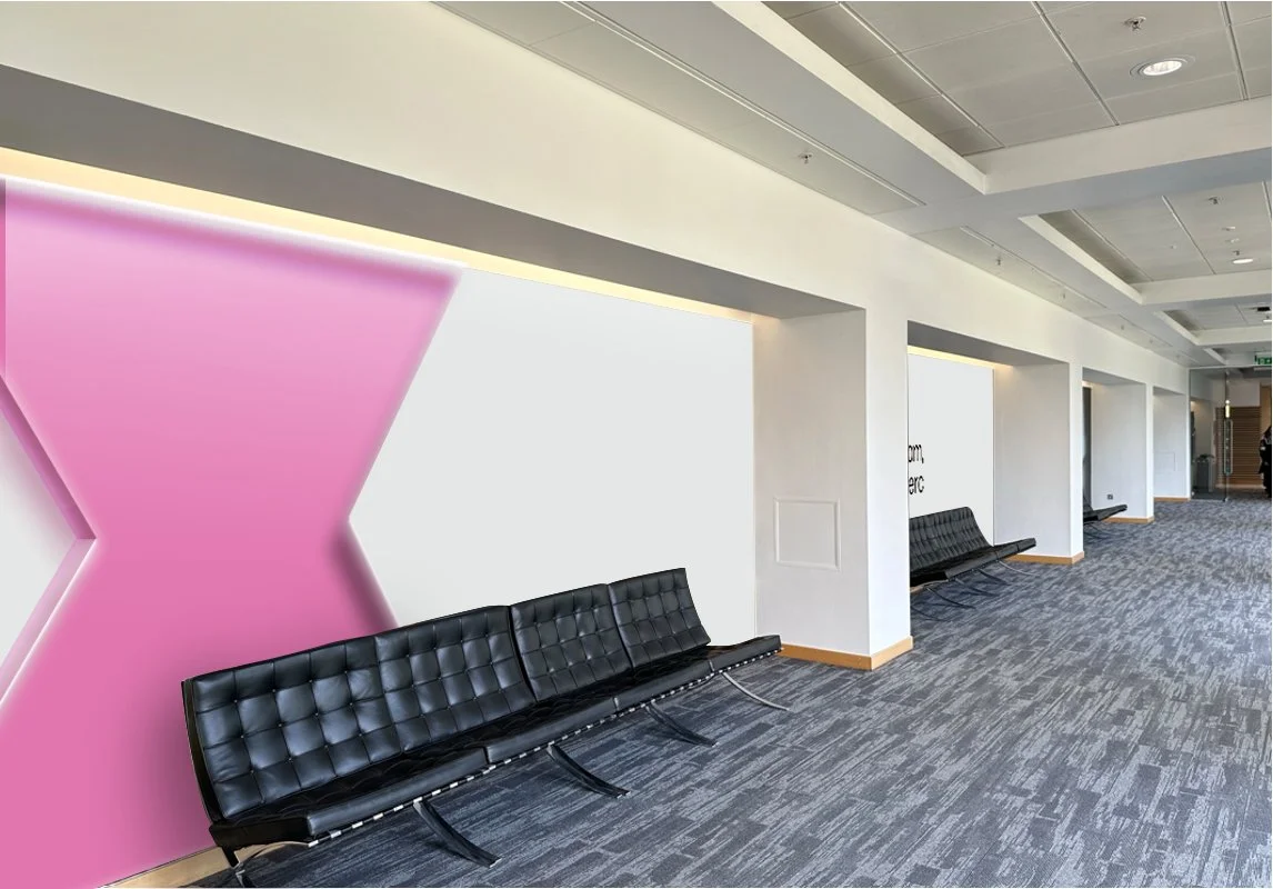 Empty airport corridor with black seating, white walls, and a pink geometric wall decoration.