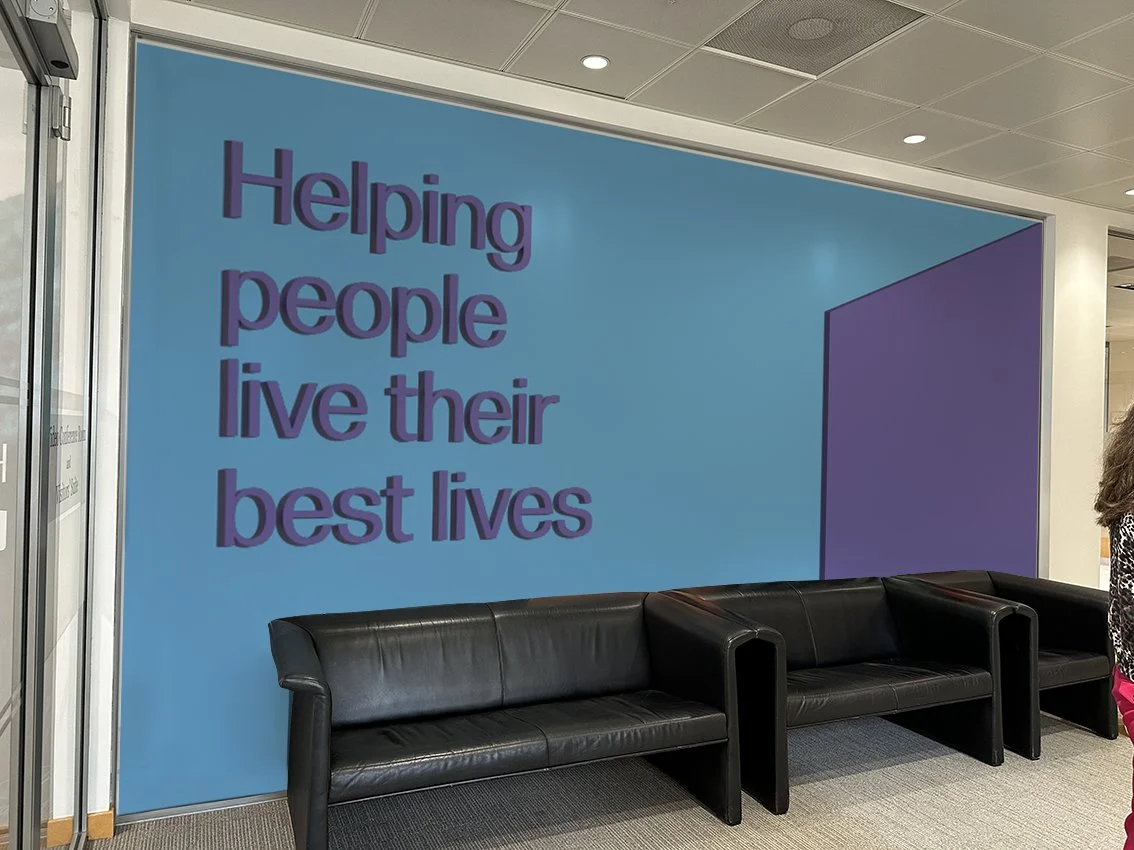 Waiting area with black leather sofas and a blue wall with the message 'Helping people live their best lives' in purple text.