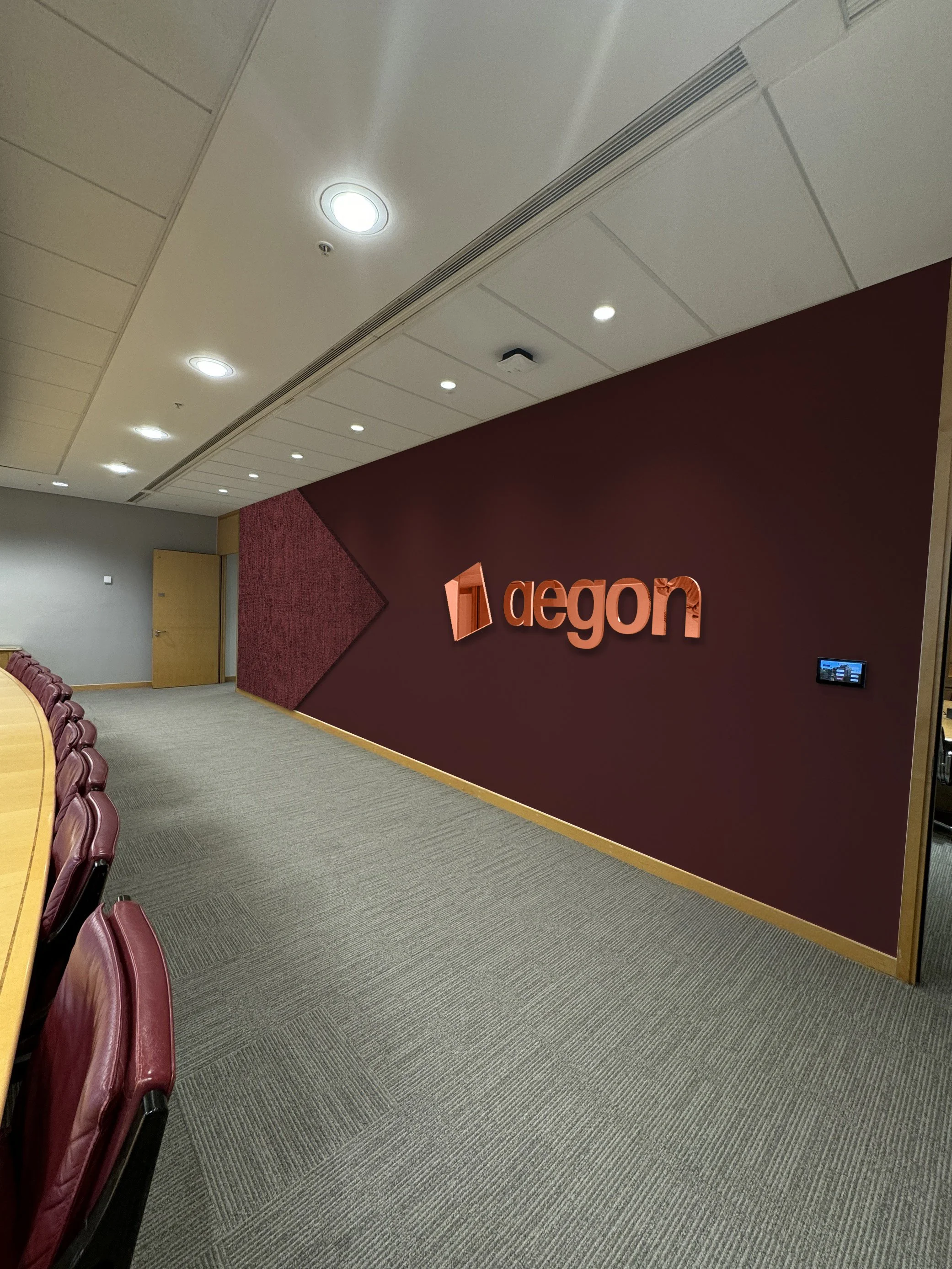 Office conference room with a burgundy accent wall displaying the Aegon logo, a door, and a row of chairs along a wooden table.
