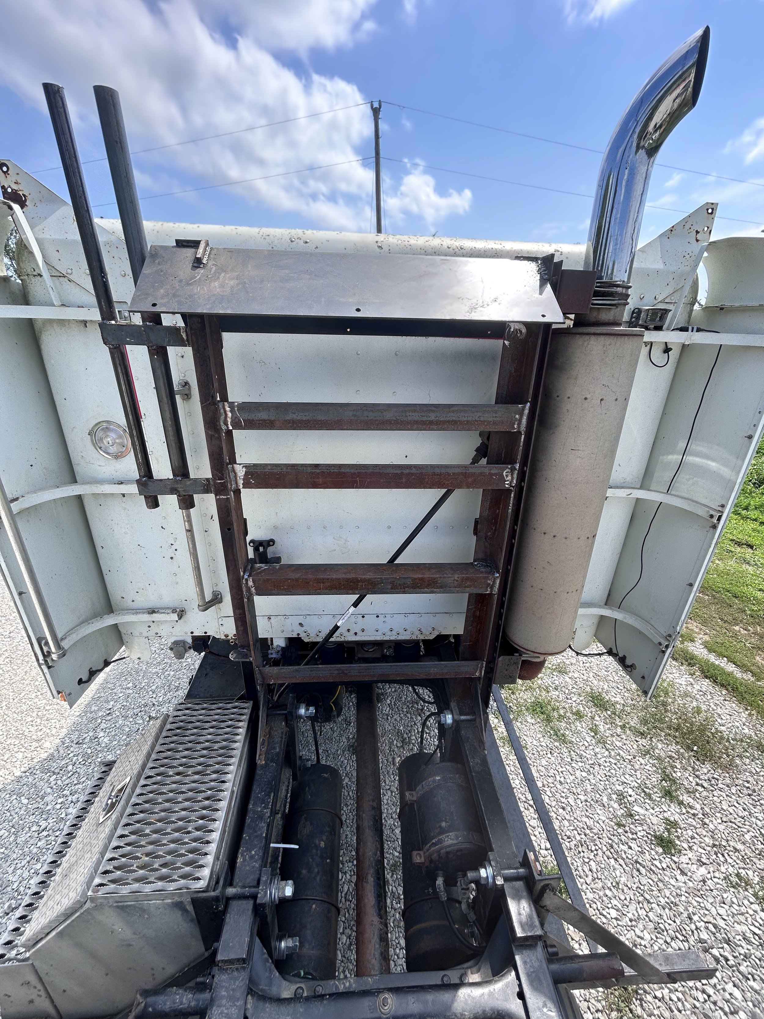 The underside of a vintage hot air balloon, showing the basket, burners, and metal framework against a blue sky with clouds.