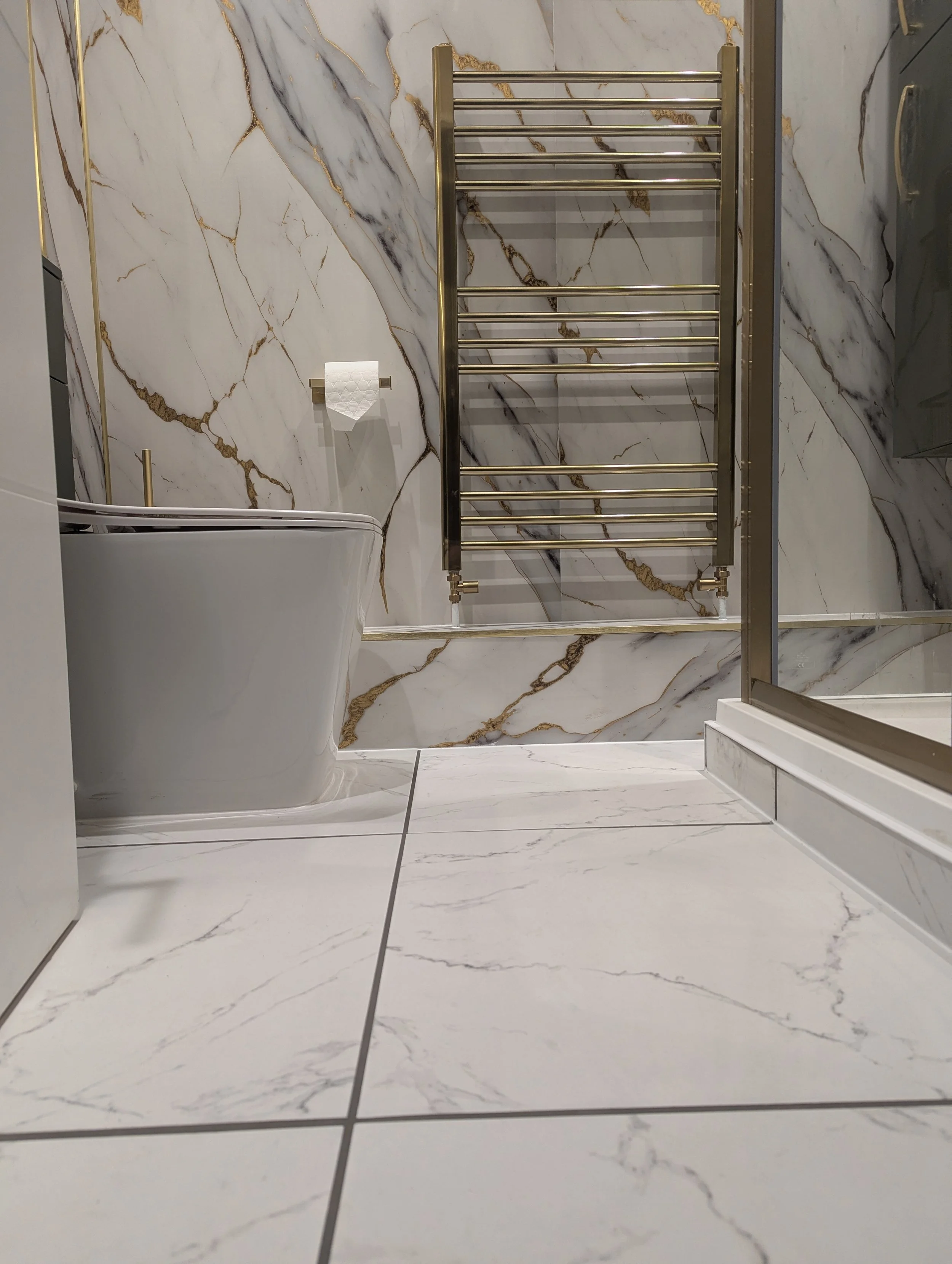 Modern bathroom with white marble tiles and gold accents, including a towel rack and a bathtub.