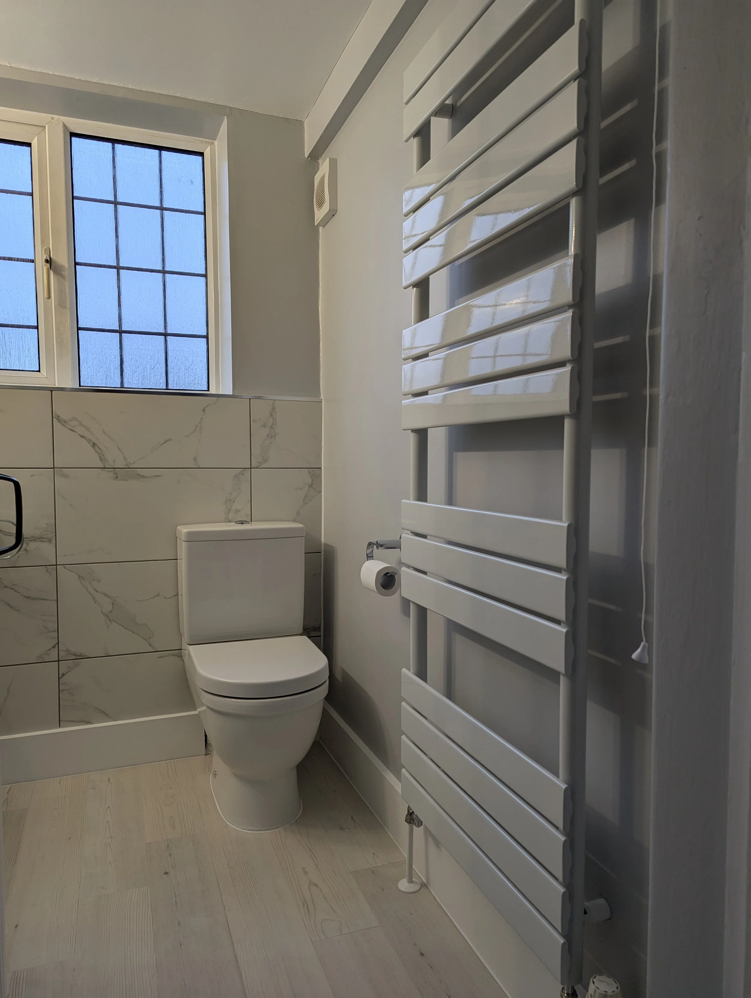 A modern bathroom with a white toilet, a frosted glass window, and a white heated towel radiator.