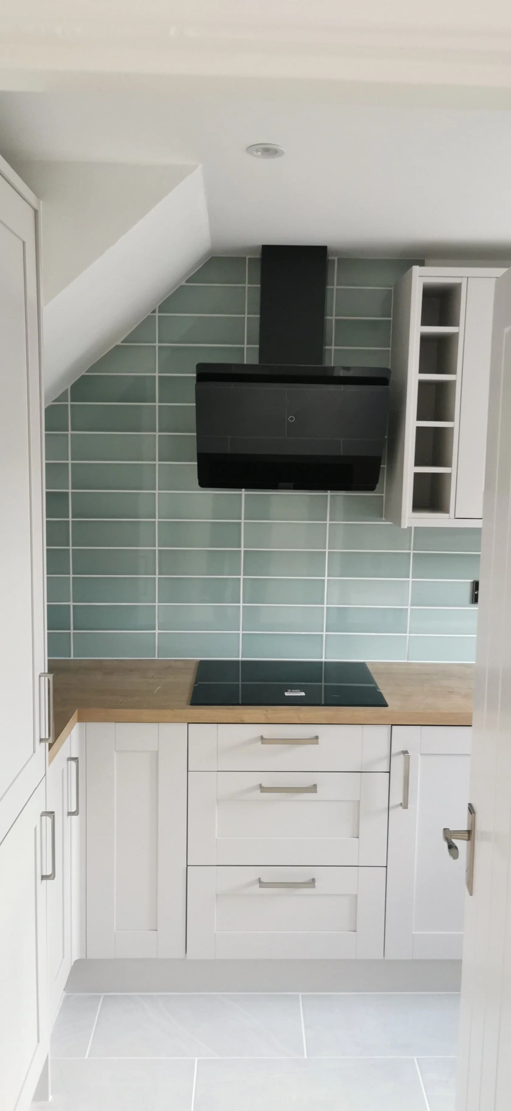 Modern kitchen with white cabinets, wooden countertop, black range hood, and light blue tile backsplash.