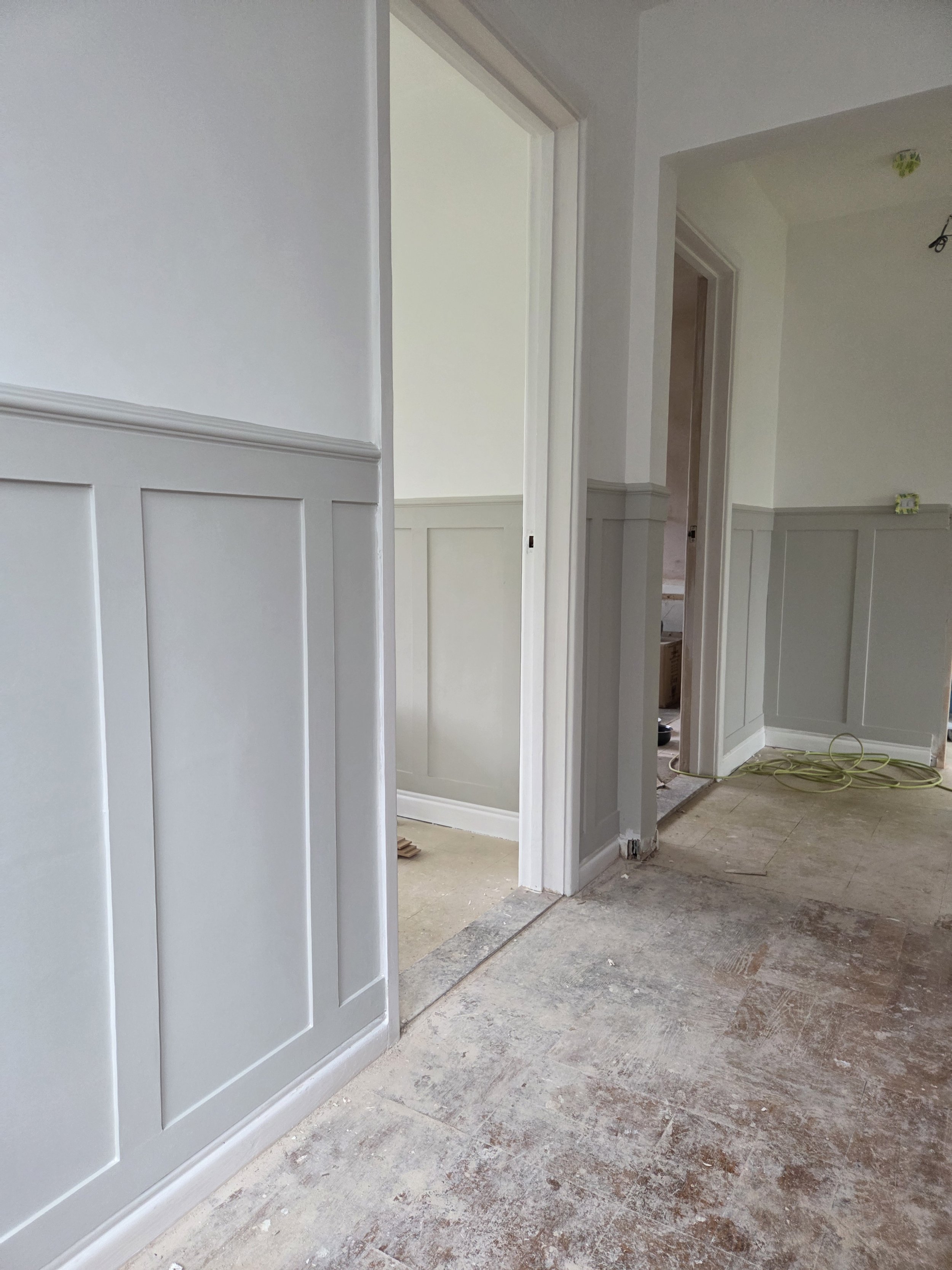 Interior of a house under renovation, showing doorways and wainscoting on the walls with a partly finished floor.