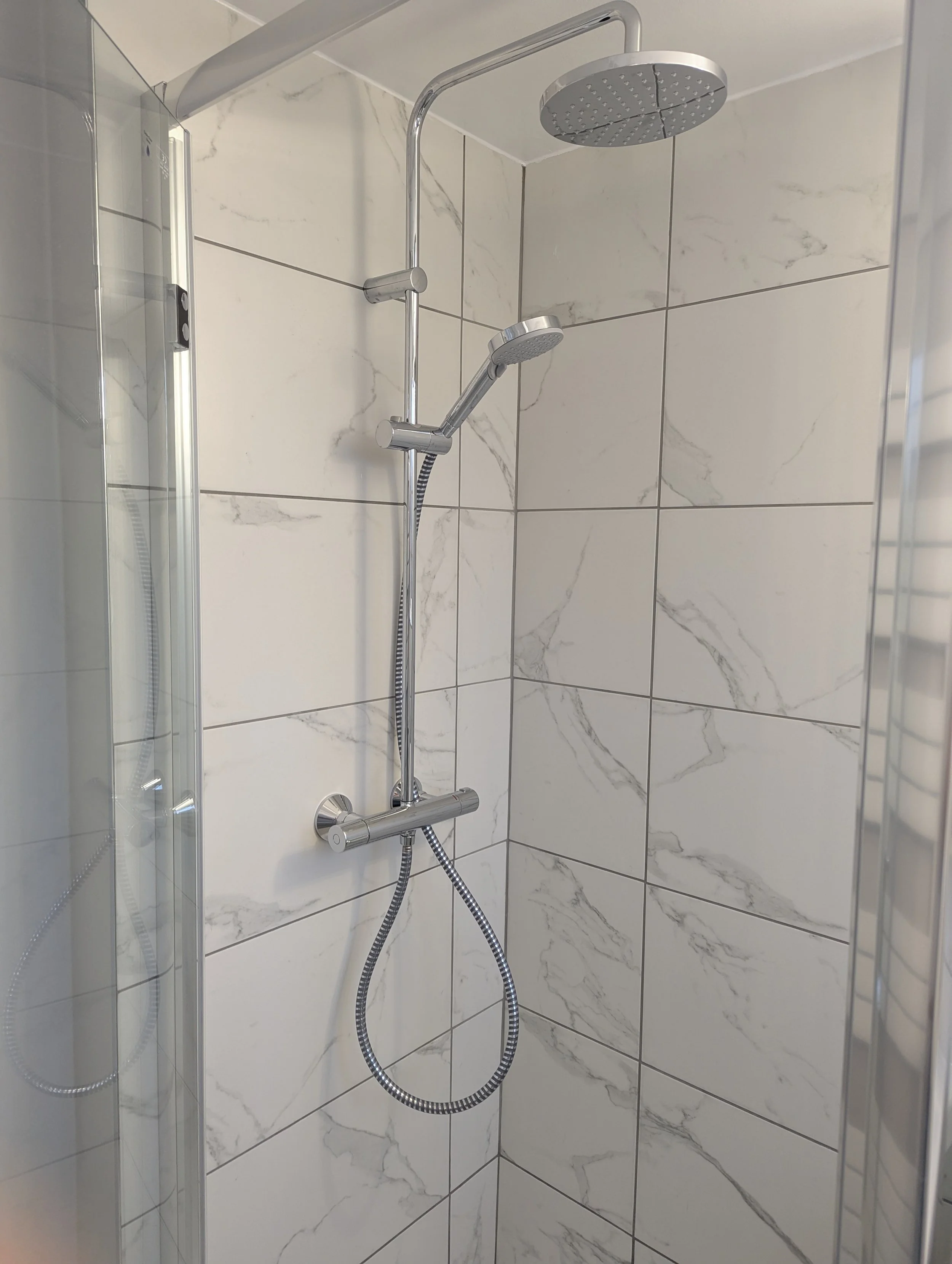 Shower with a rain shower head and a handheld shower head mounted on a tiled wall.