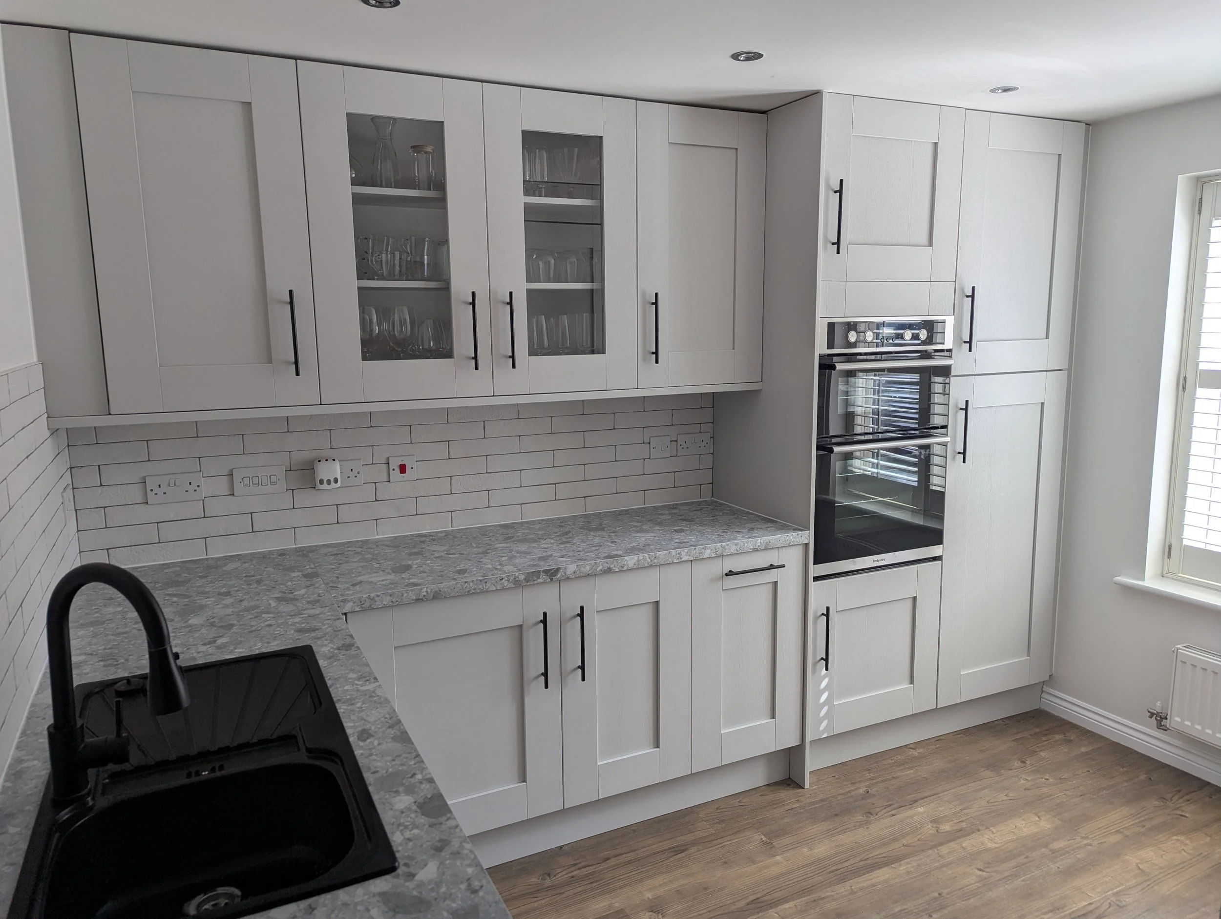 Modern kitchen with white cabinets, granite countertop, built-in double oven, black sink, and wood flooring.