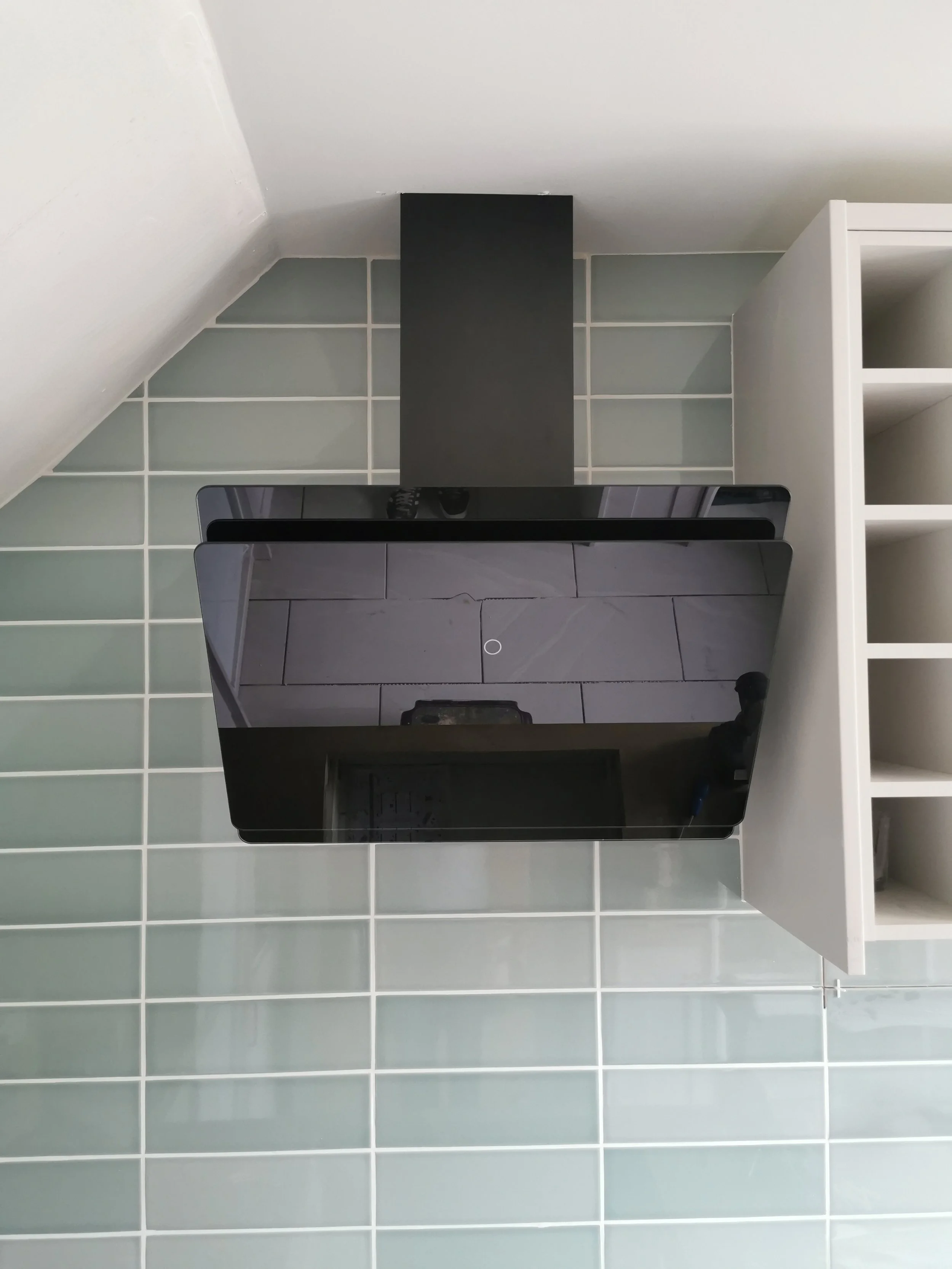 Black kitchen range hood mounted above a gray tiled backsplash and white cabinets on the right wall.