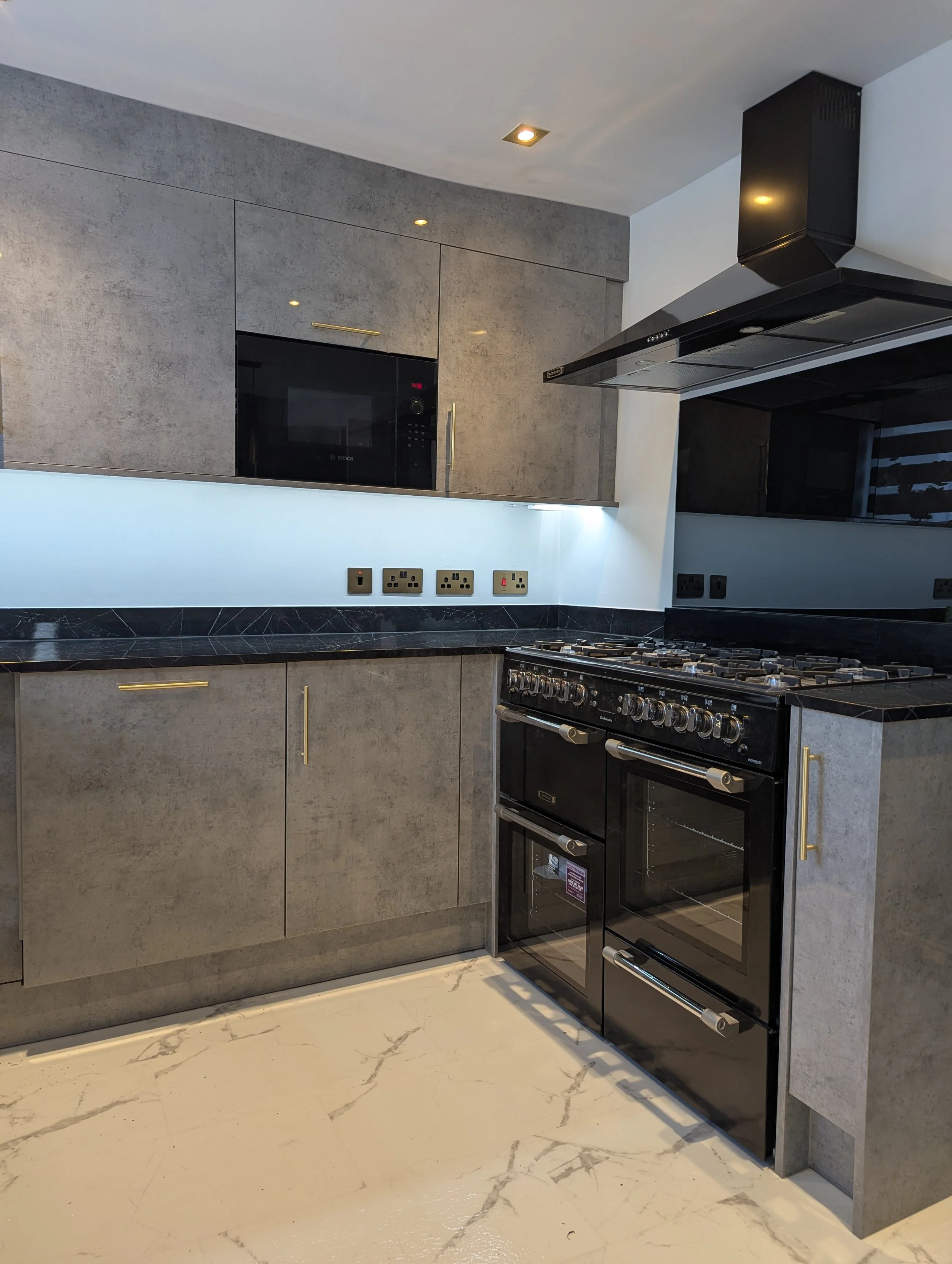 Modern kitchen with black oven, gray cabinets, black marble countertop, and multiple electrical outlets.