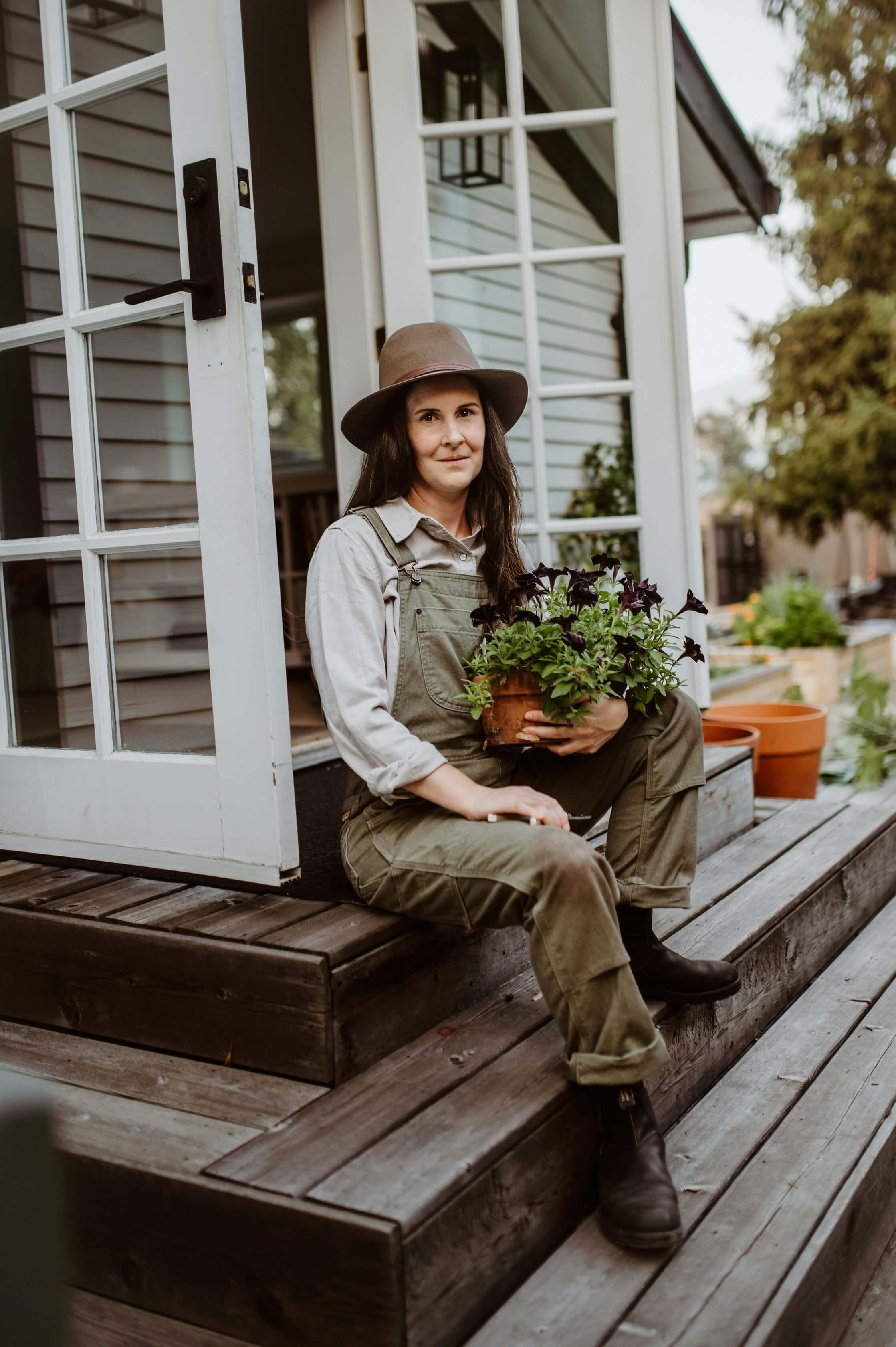 Woman with dark hair sitting on steps and holding a plant