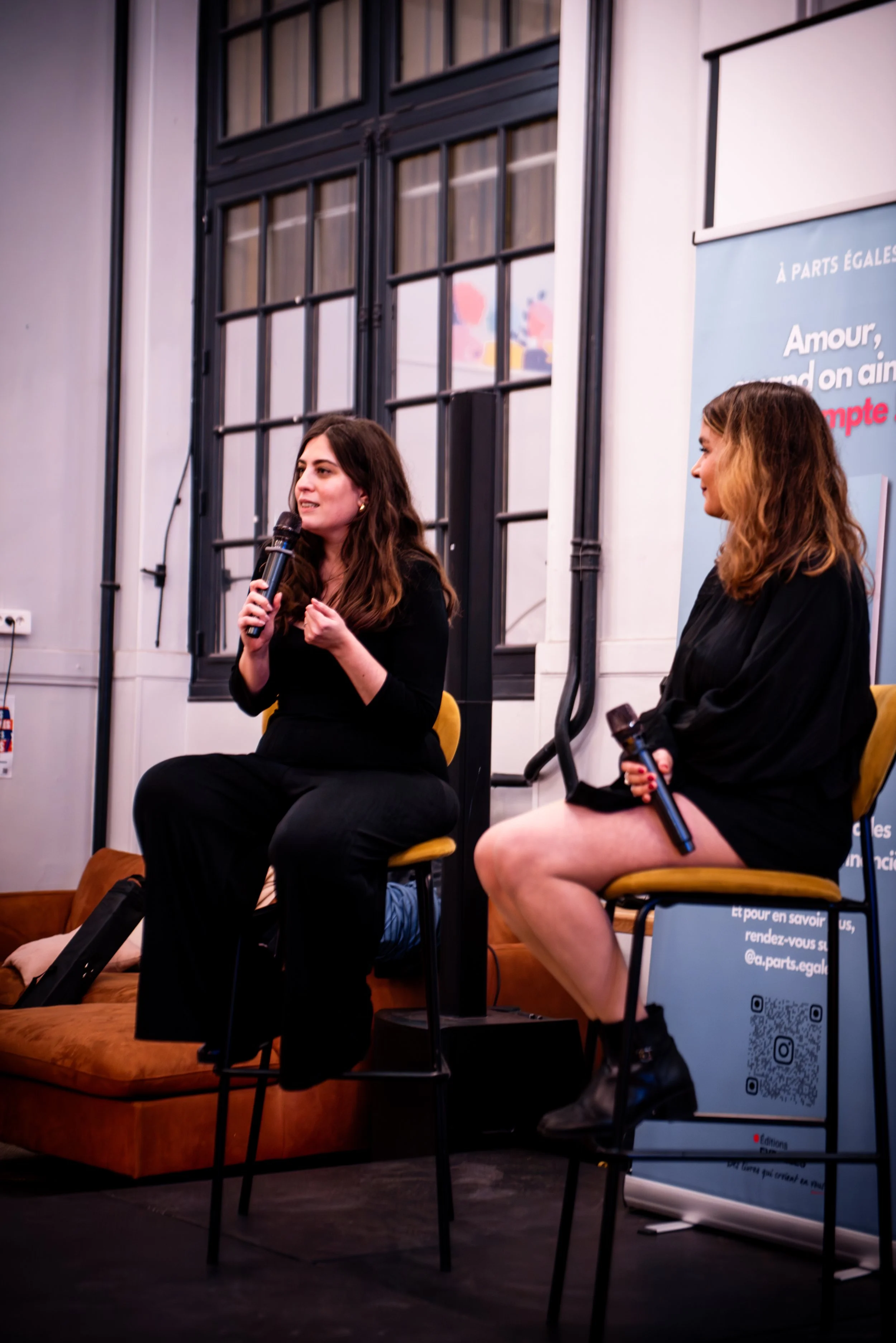 Deux femmes parlent lors d'une discussion ou d'une interview, tenant des microphones dans un environnement intérieur.