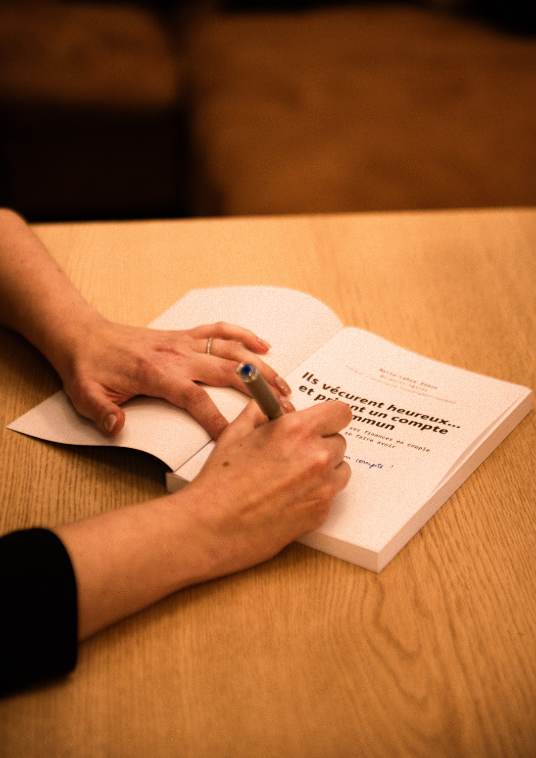 Une personne écrit dans un livre posé sur une table en bois.