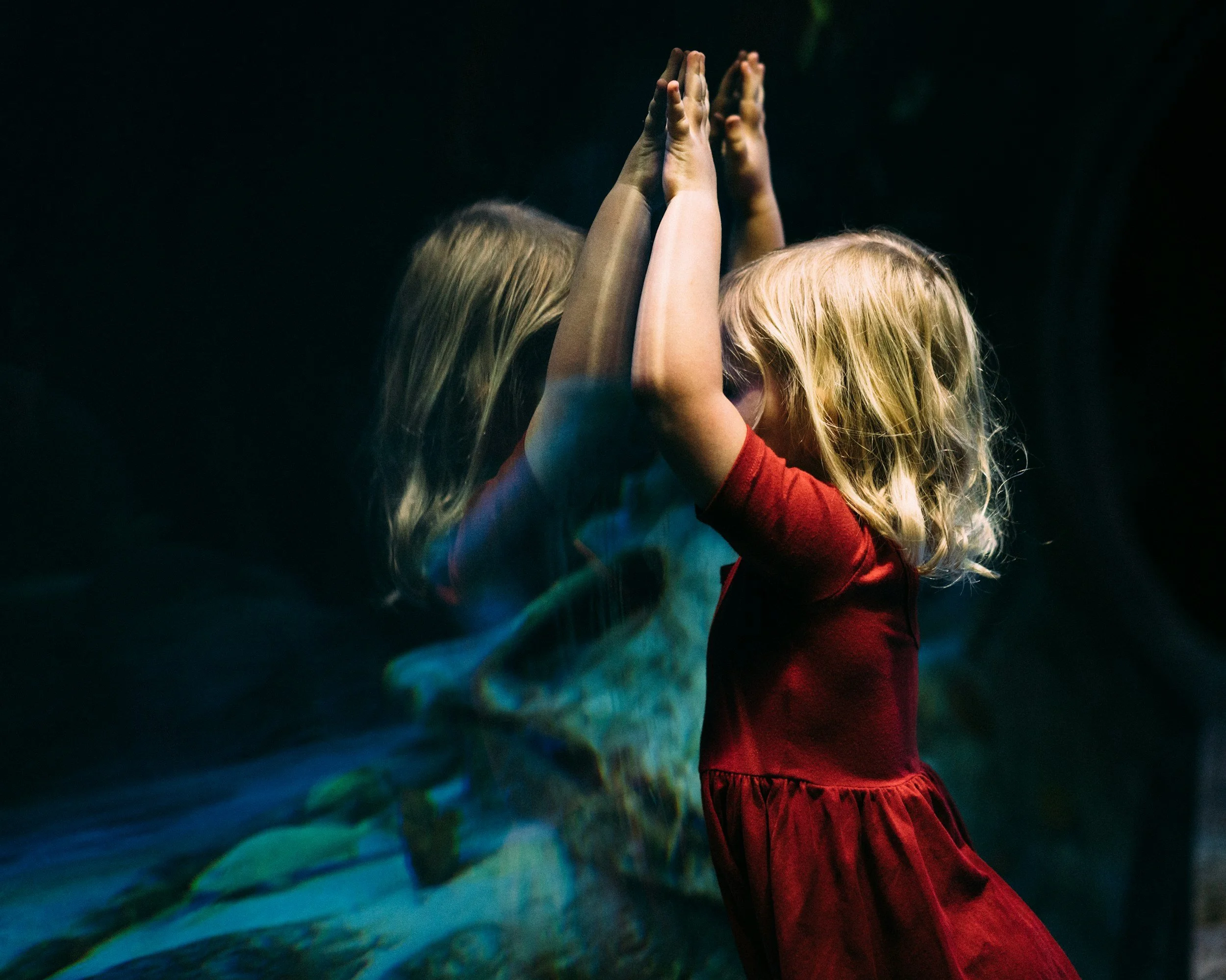 Two young girls with curly blonde hair giving each other a high five indoors, with a dark background.
